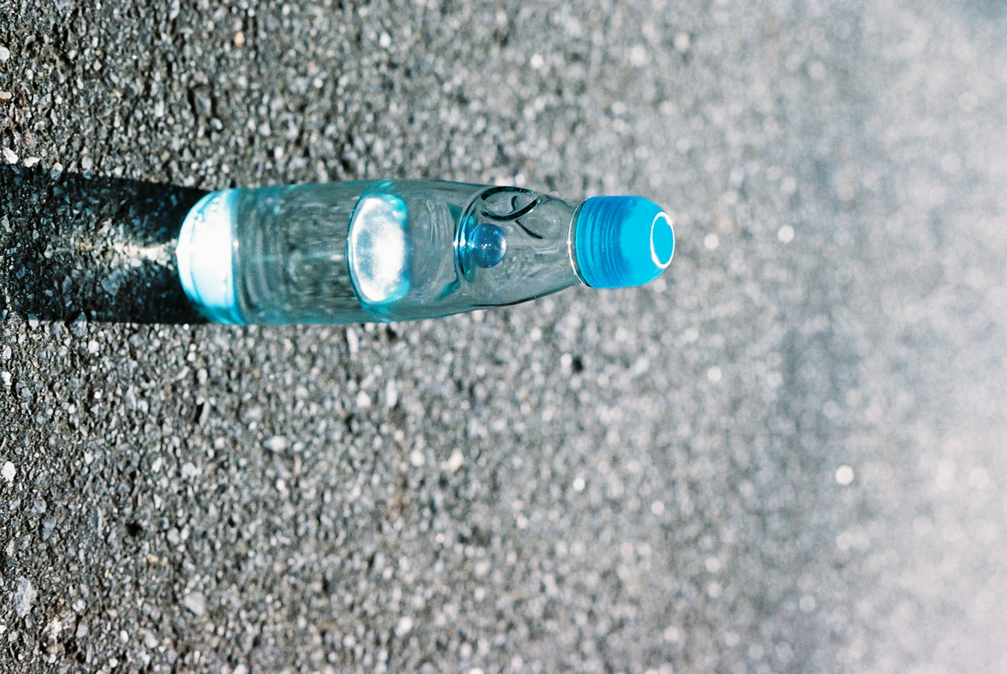 Una bottiglia d'acqua trasparente con un tappo blu che giace sull'asfalto