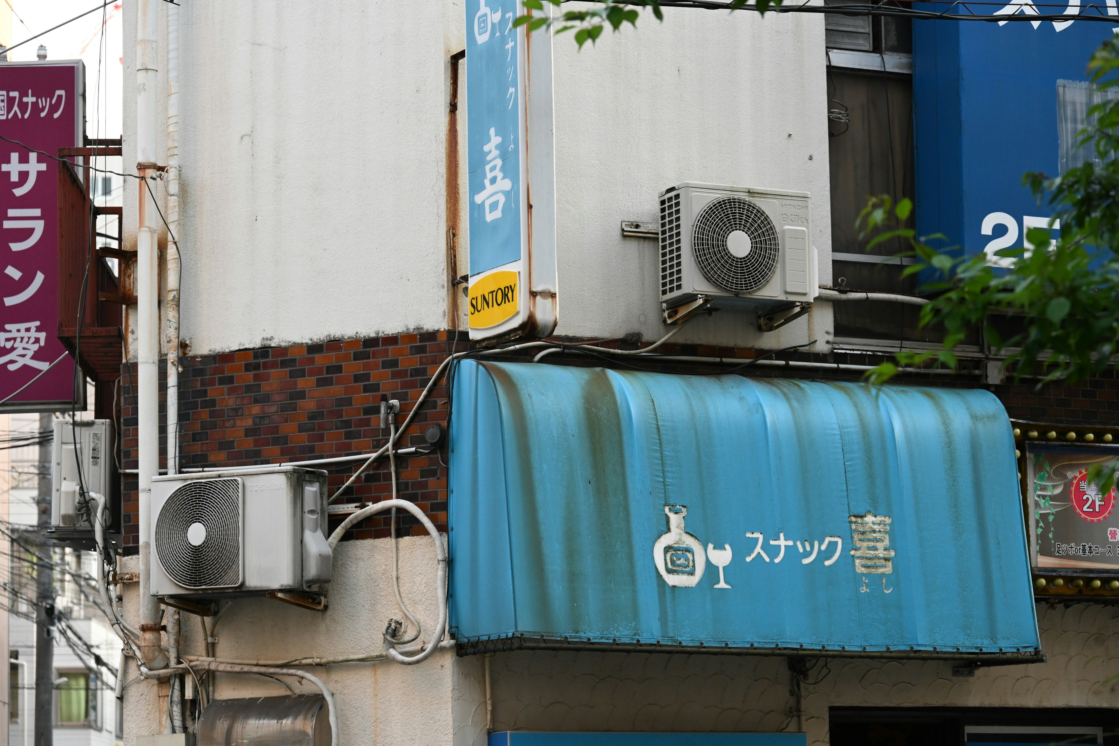 青い屋根の下にあるスナックの看板とエアコン