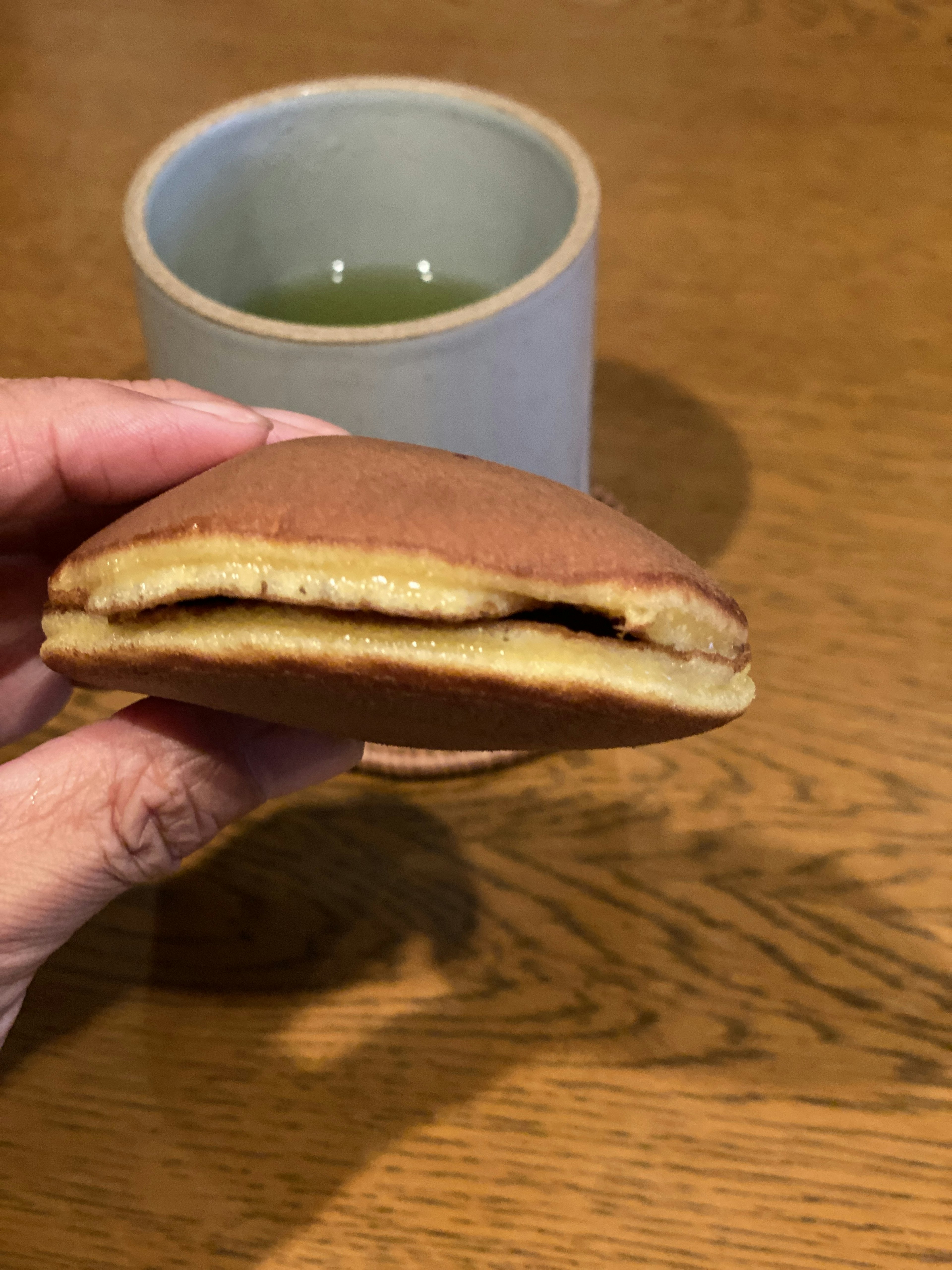 A hand holding a Japanese confection with green tea in the background