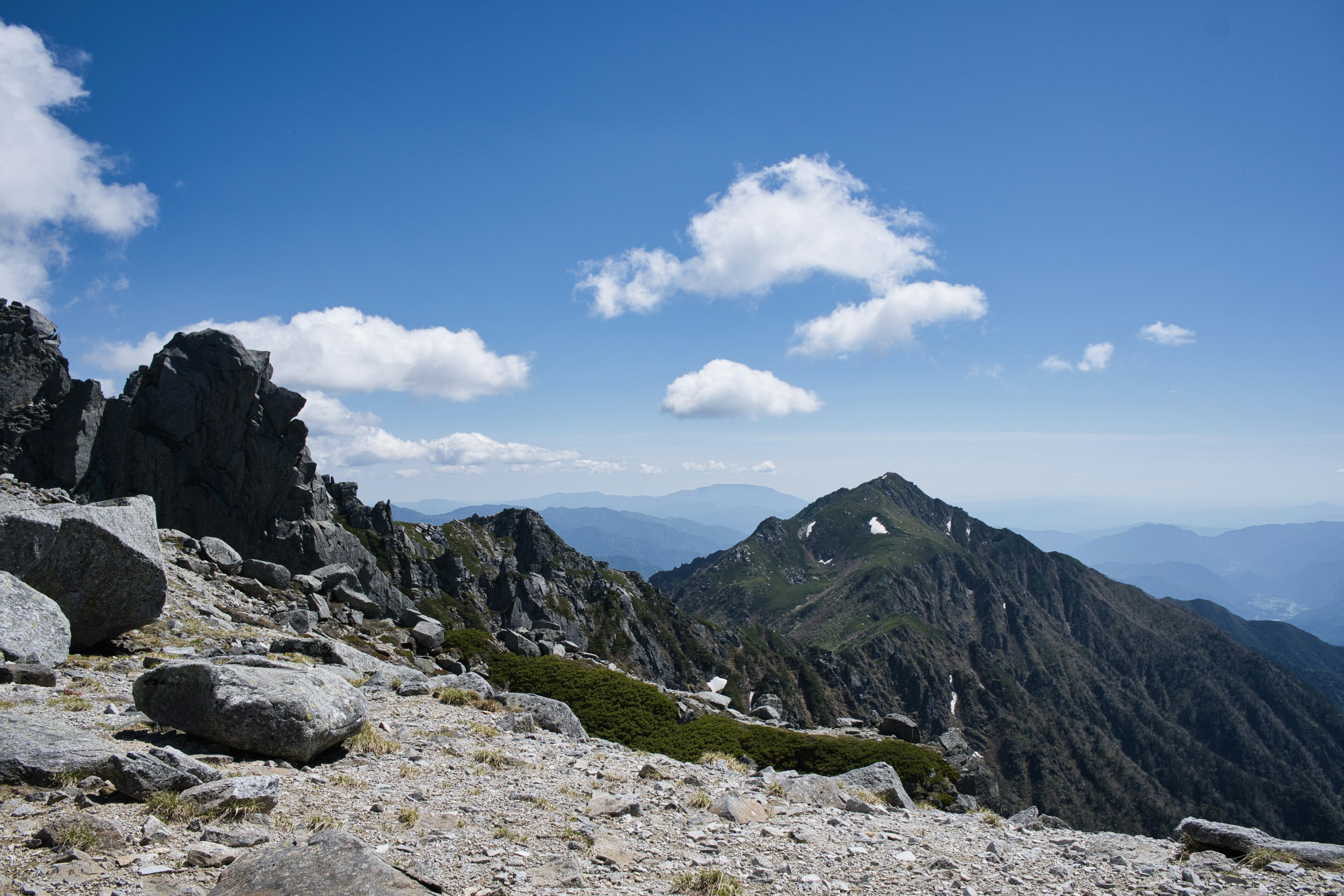 Berglandschaft unter blauem Himmel mit großen Felsen und grünem Gras