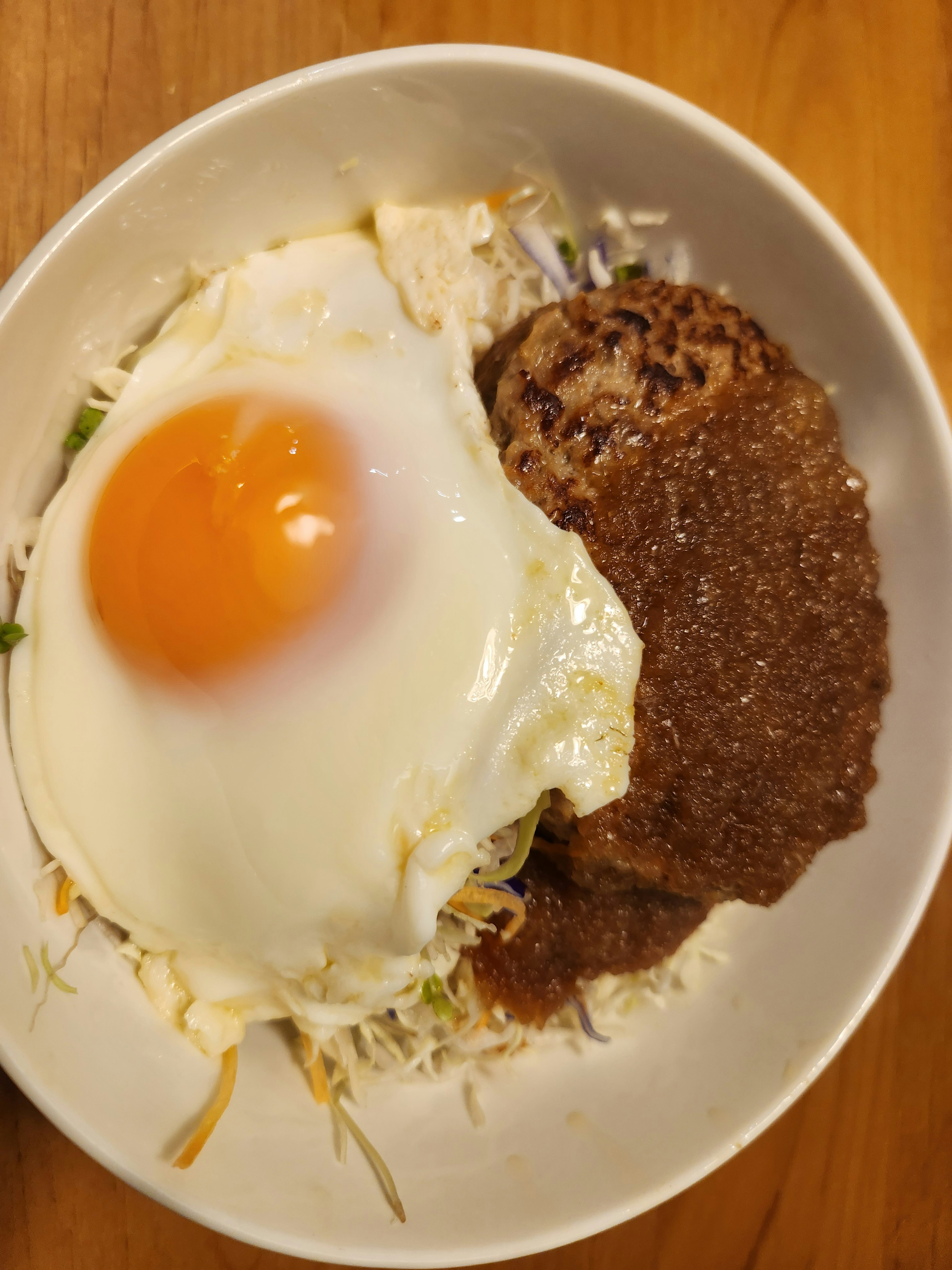 A white plate with rice topped with a fried egg and a sauce-covered hamburger steak