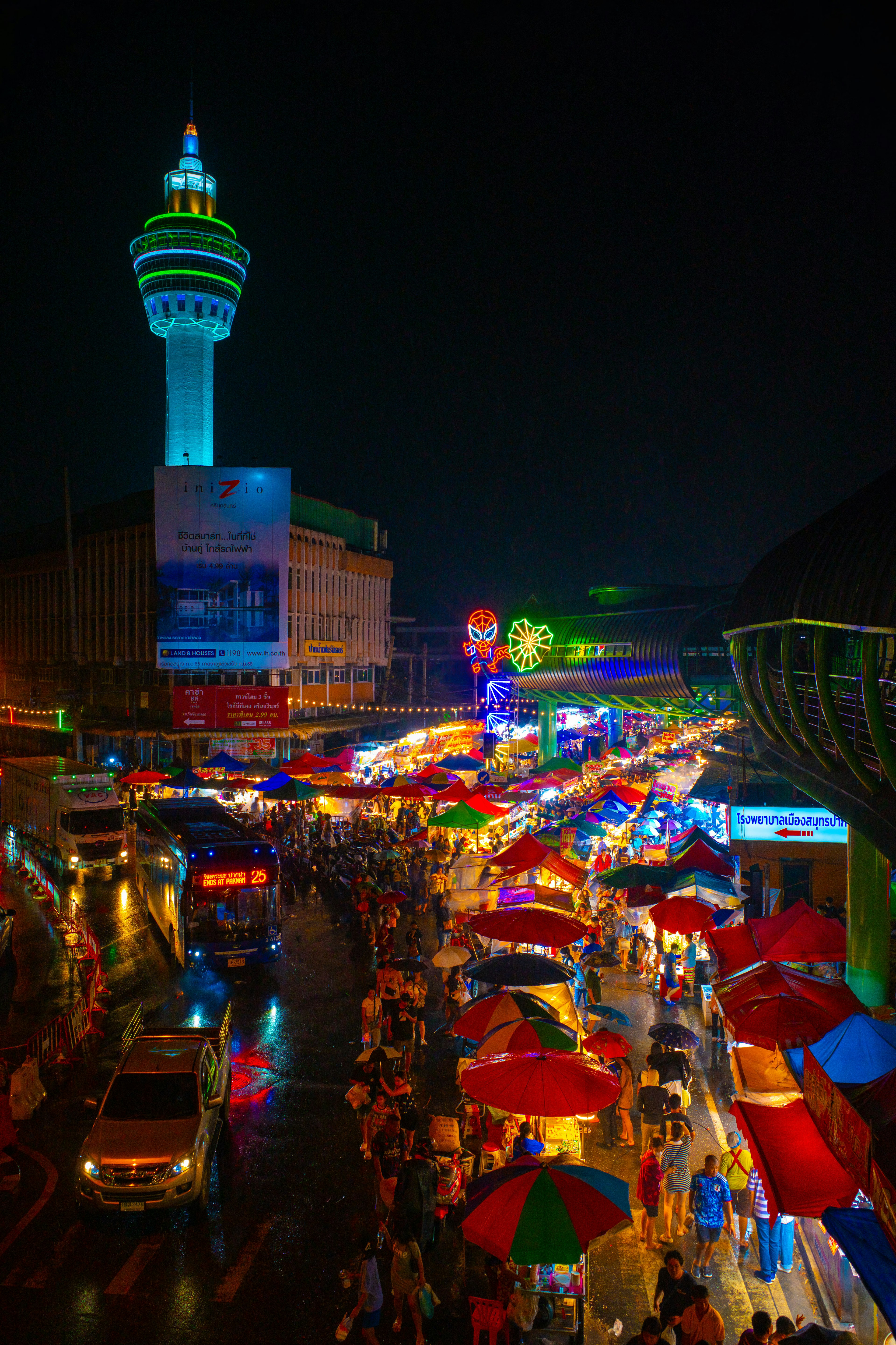 Mercado nocturno bullicioso con paraguas coloridos y torre iluminada