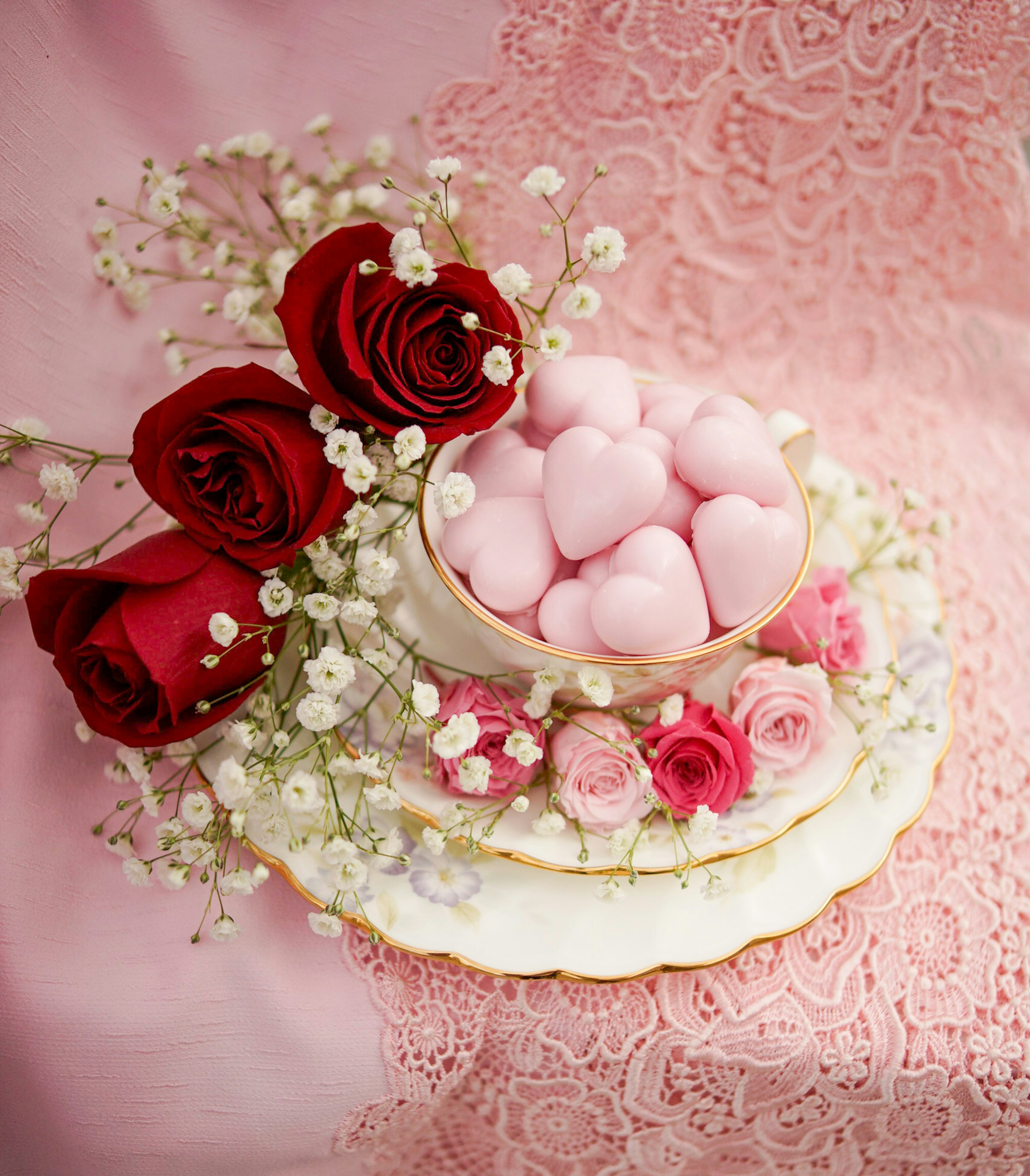 Une belle assiette ornée de douceurs en forme de cœur entourée de roses rouges et de dentelle rose