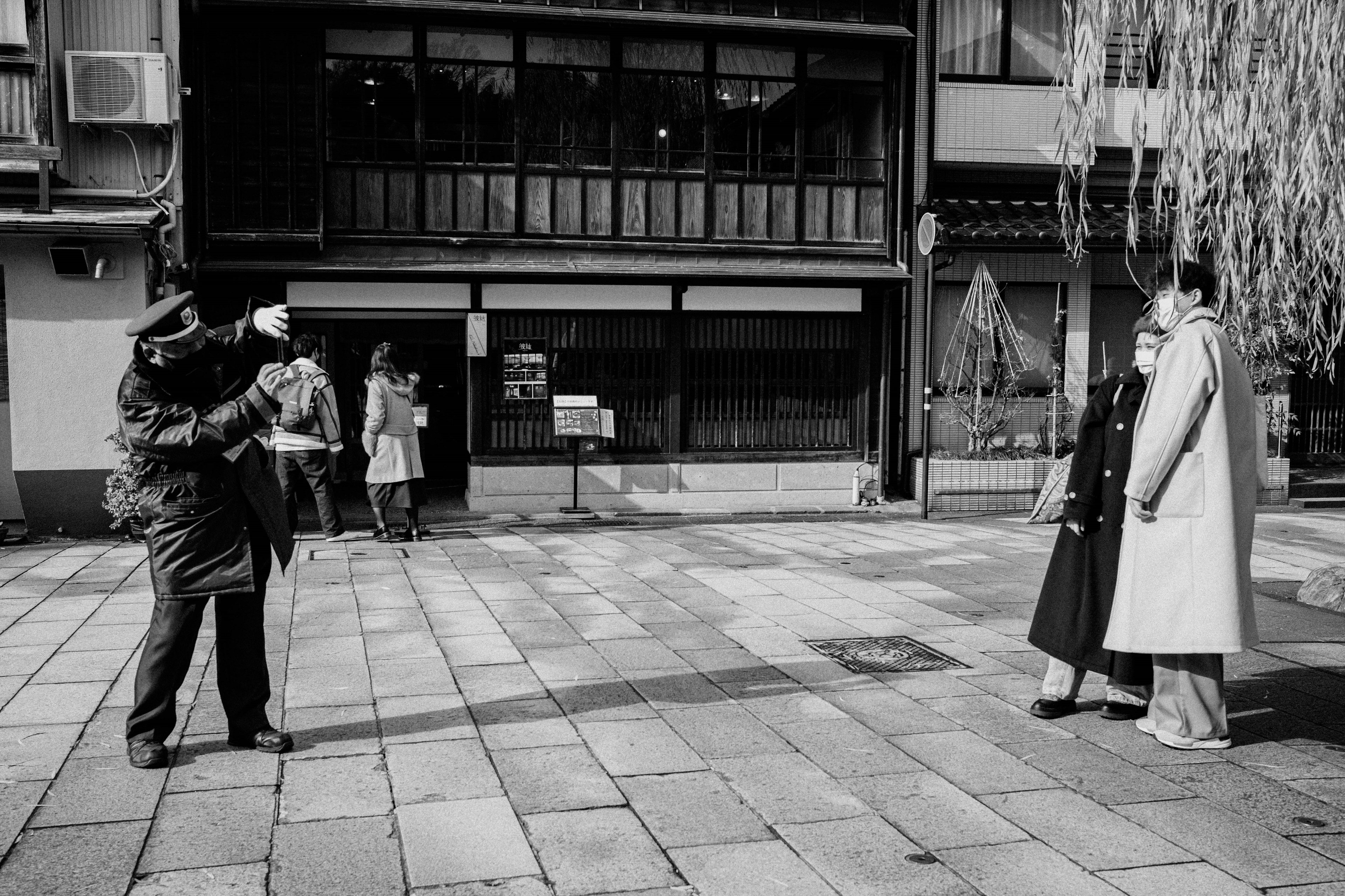 Una escena de calle en blanco y negro con un hombre sosteniendo una cámara y mujeres cerca