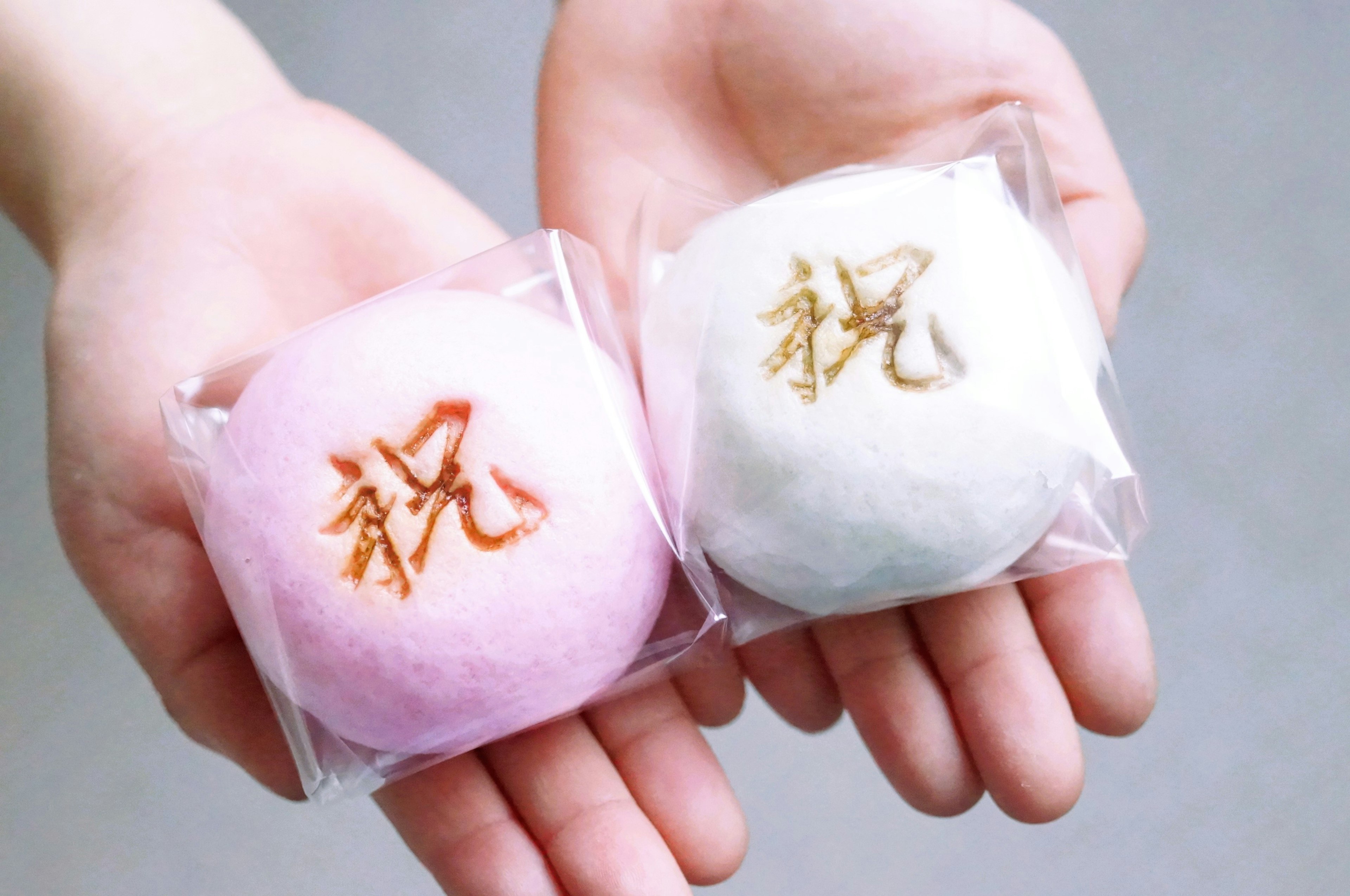 Dos dulces tradicionales japoneses en rosa y blanco sostenidos en manos con el carácter para celebración