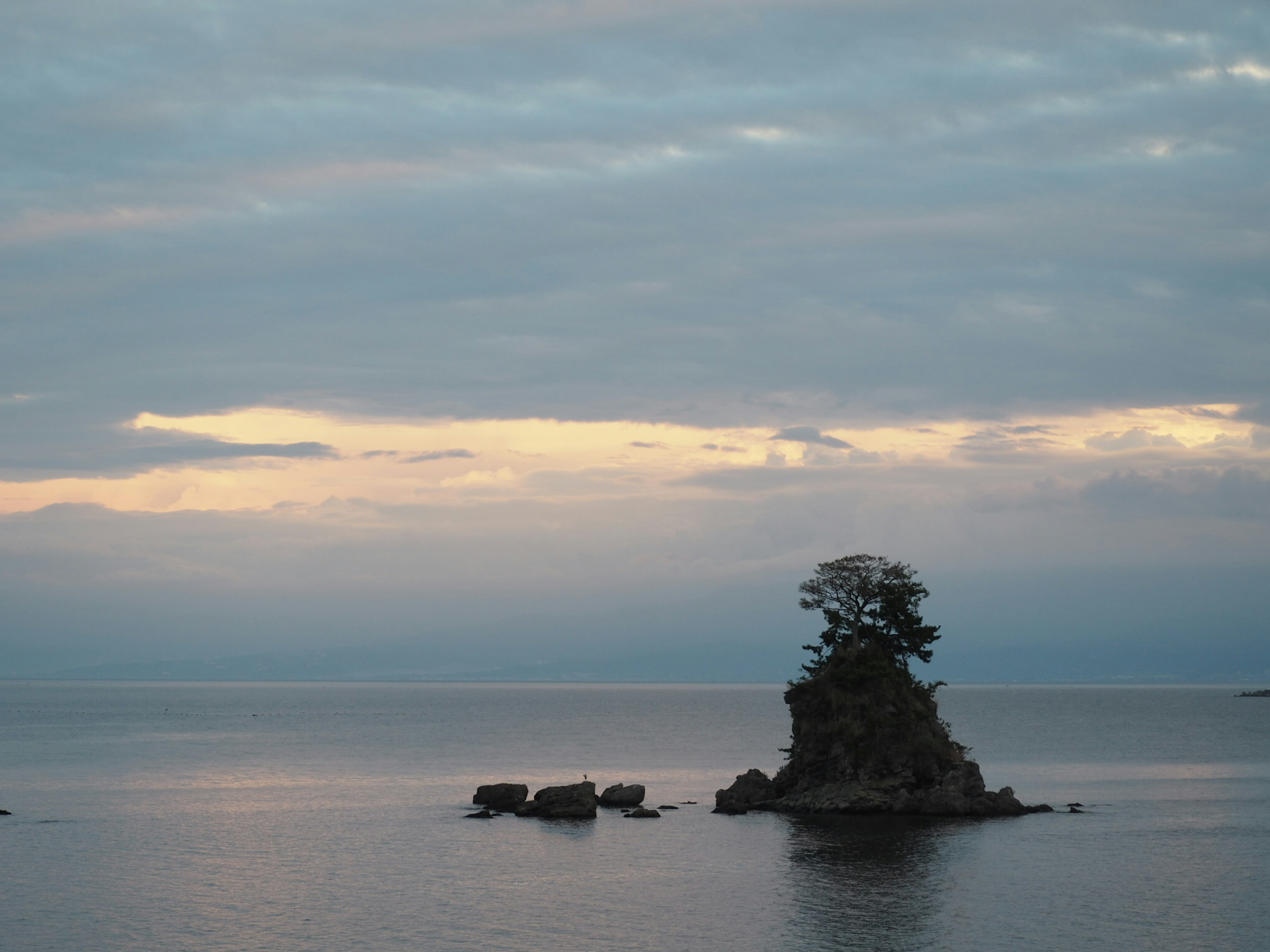 A small island surrounded by calm water with a soft twilight sky