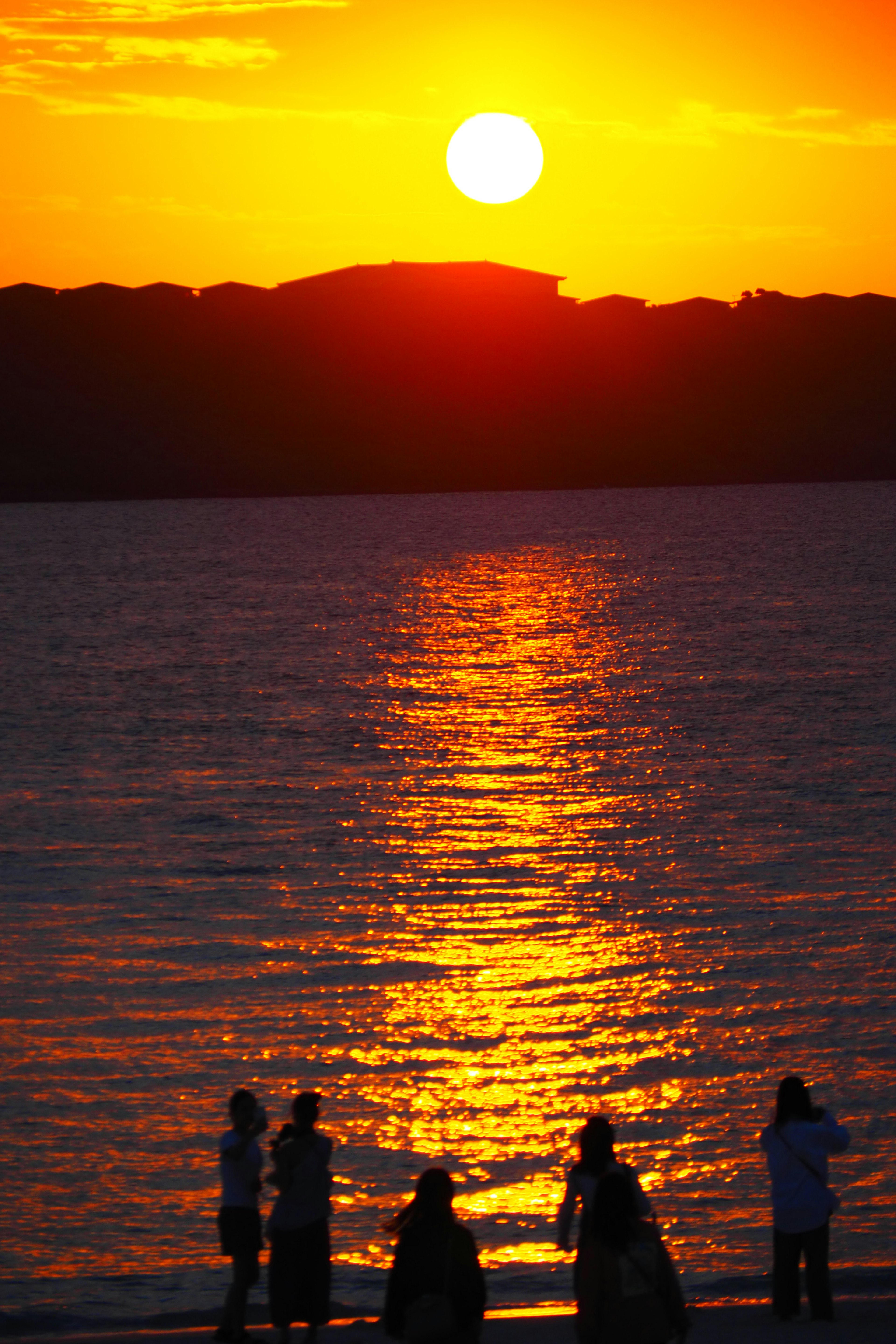 Siluetas de personas junto al mar al atardecer con reflejos dorados