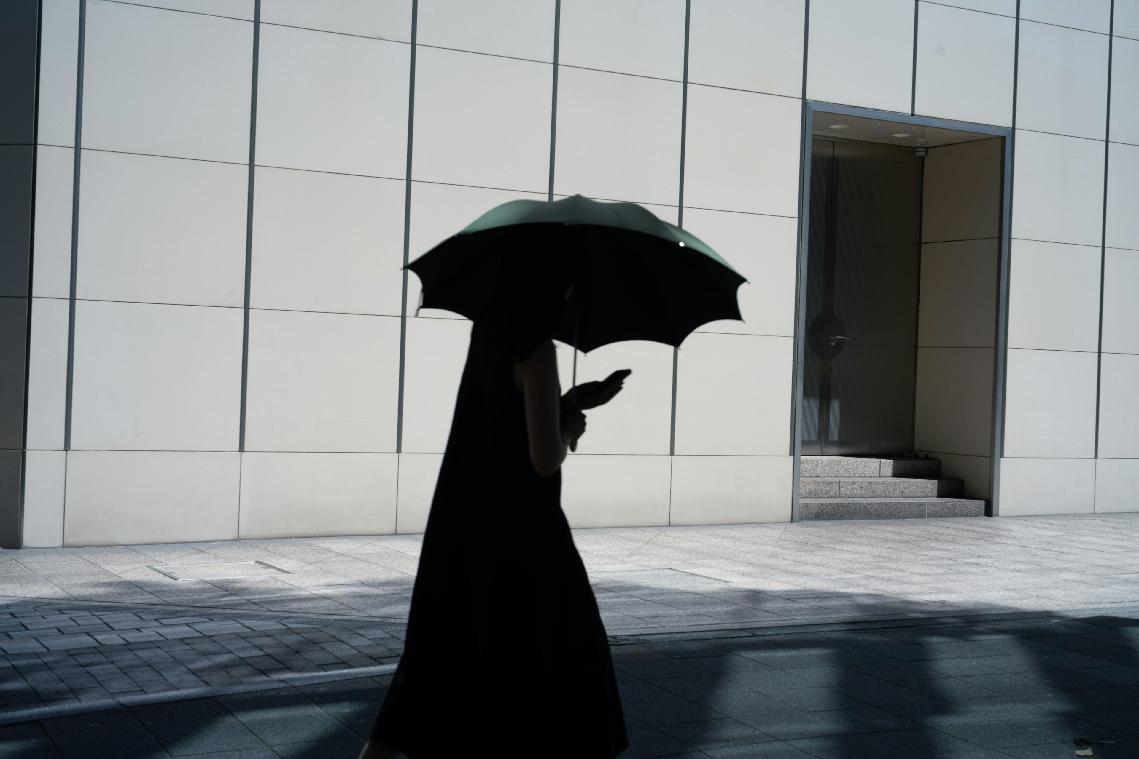 Silhouette of a woman holding an umbrella walking in front of a modern building