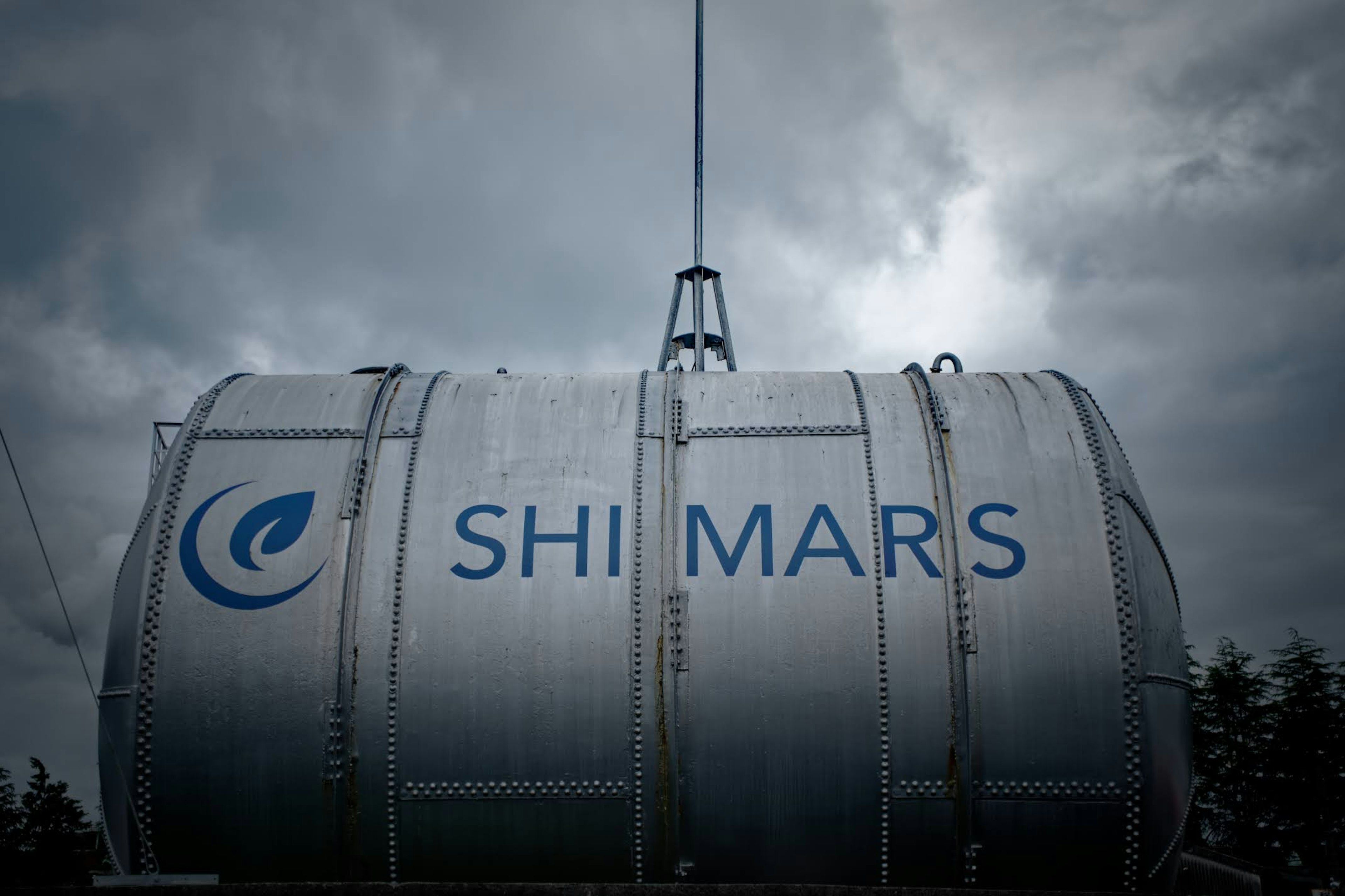 Metalltank mit SHI MARS-Logo, der gegen einen dunklen, bewölkten Himmel angehoben wird