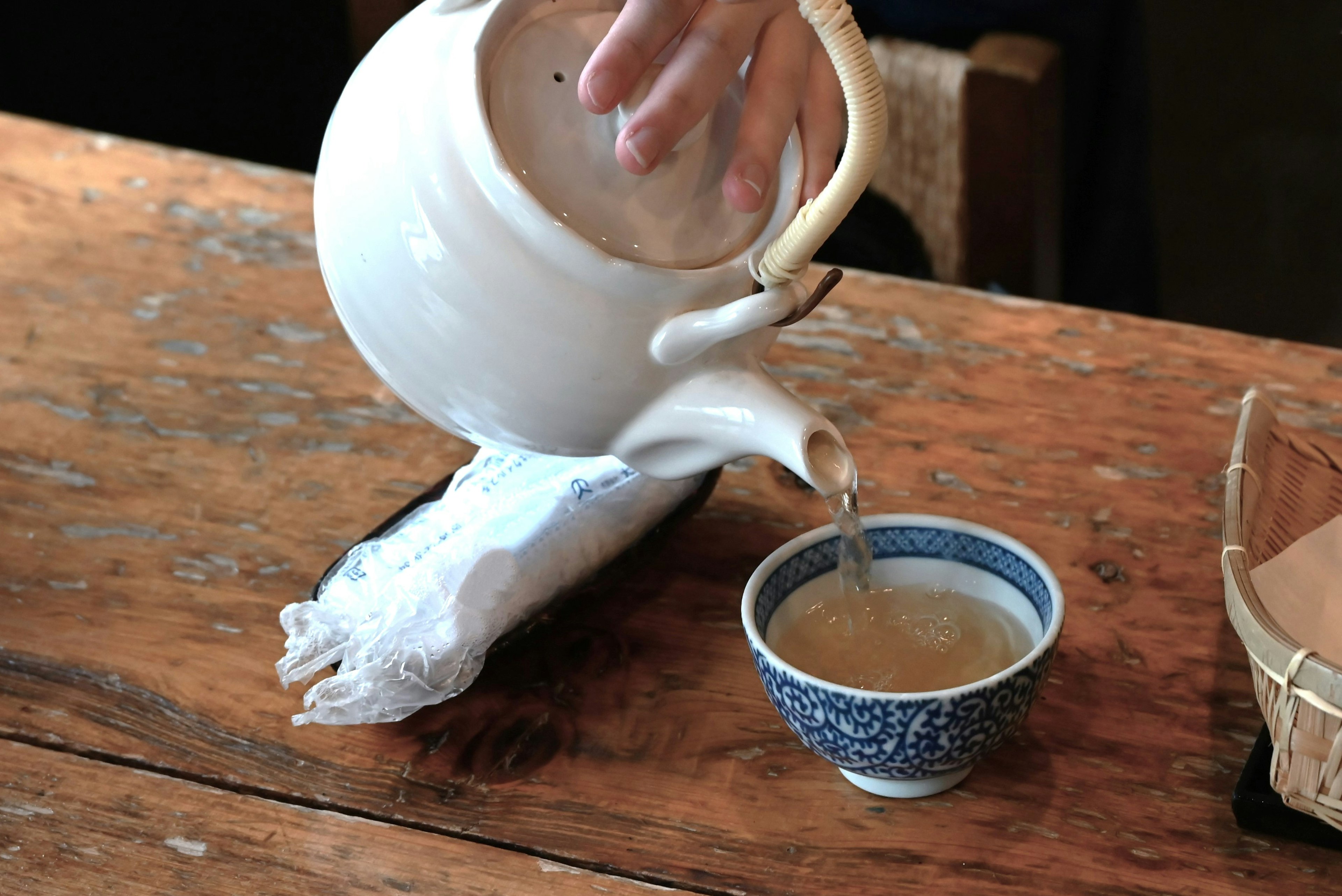 Eine weiße Teekanne gießt Tee in eine blau gemusterte Tasse