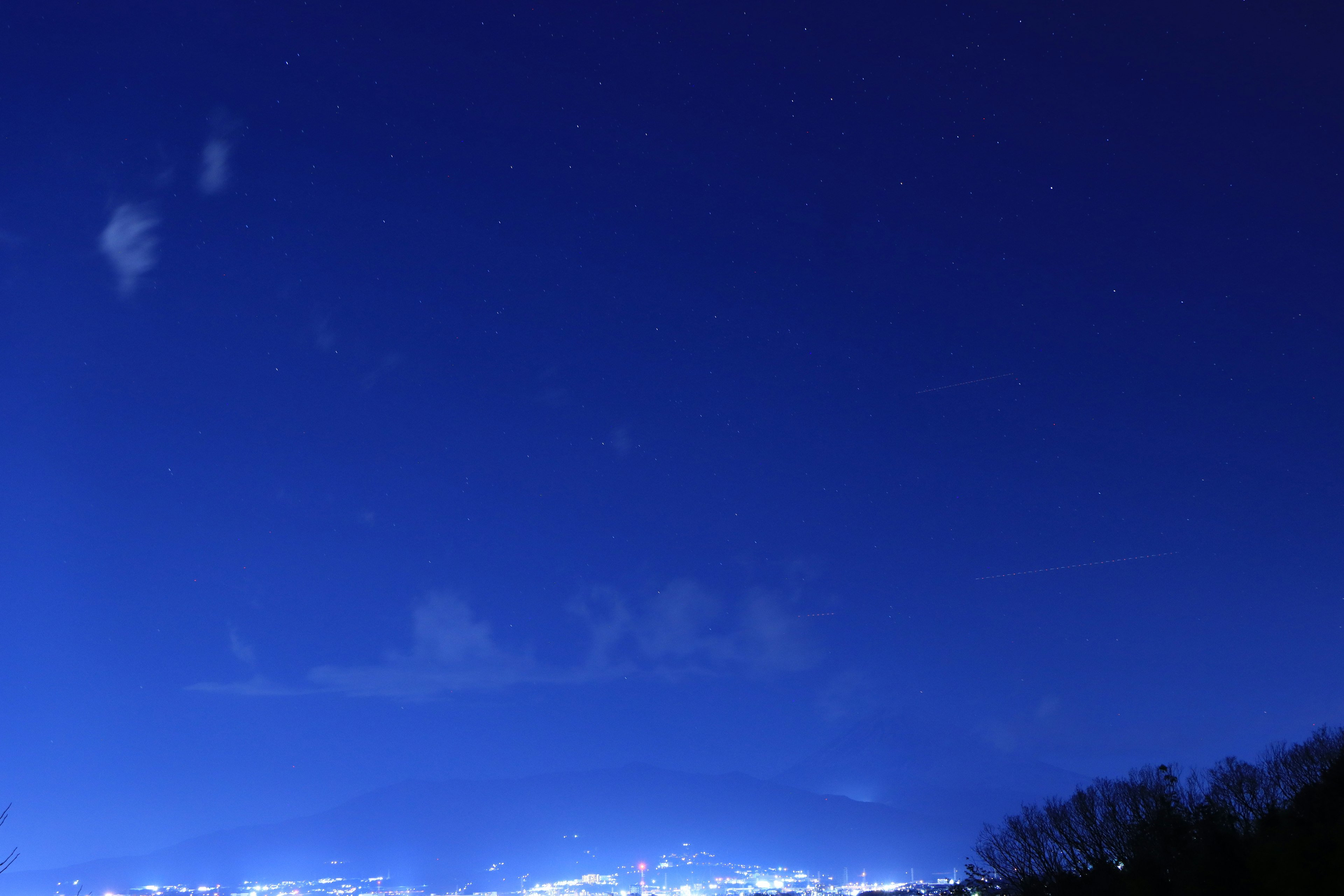 Cielo nocturno con estrellas brillantes contra un fondo azul y luces de la ciudad