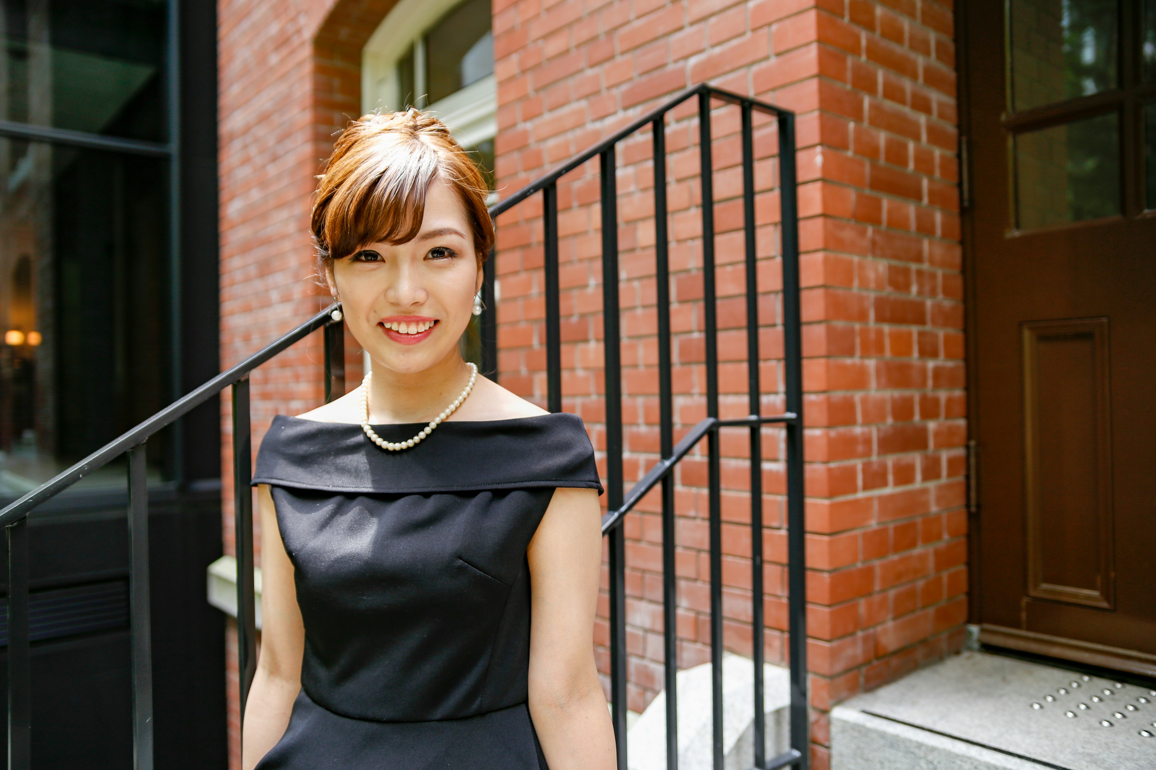 A woman in a beautiful black dress standing in front of a brick building