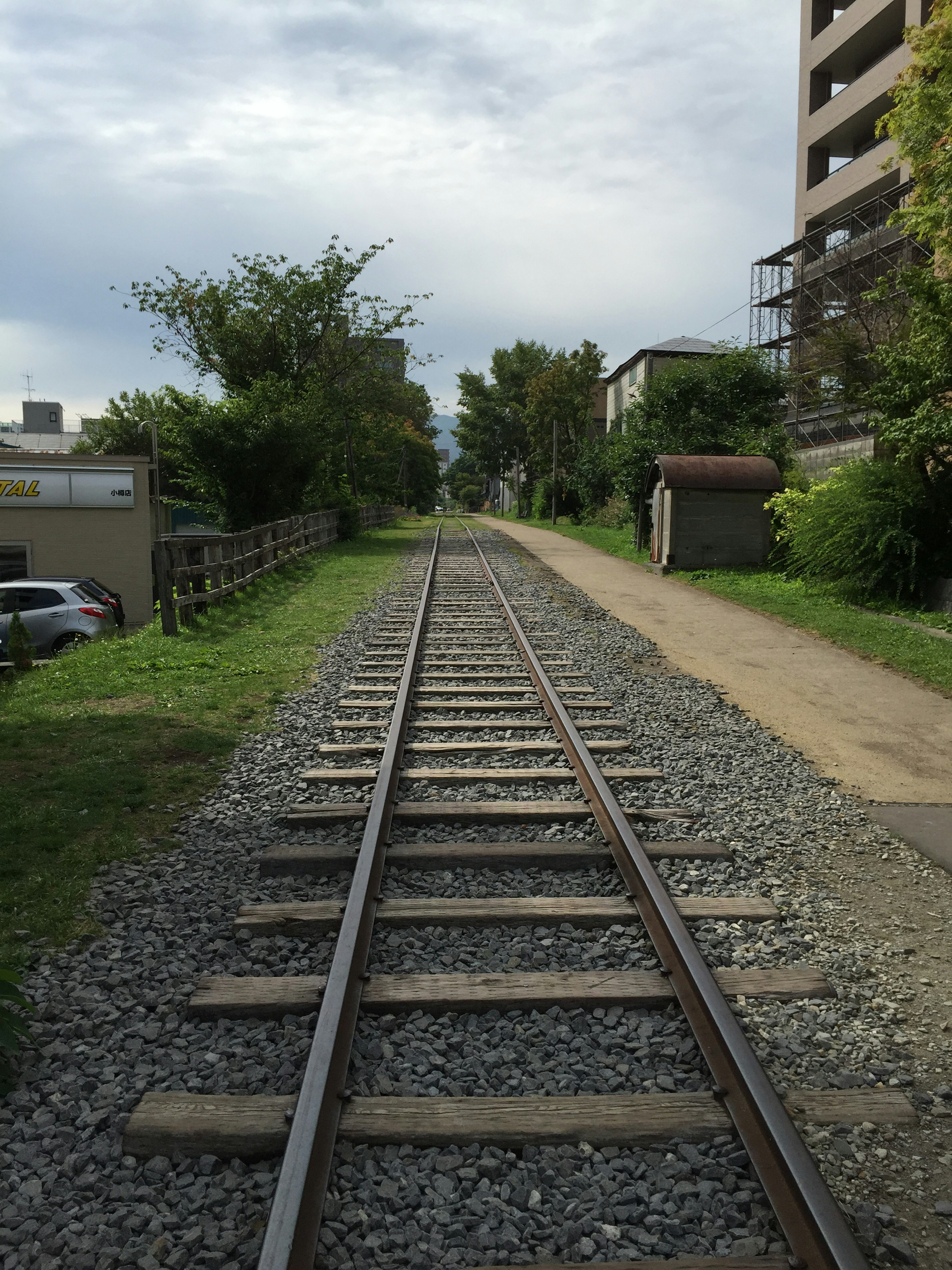 Eine perspektivische Ansicht von Bahngleisen umgeben von Grün und Gebäuden