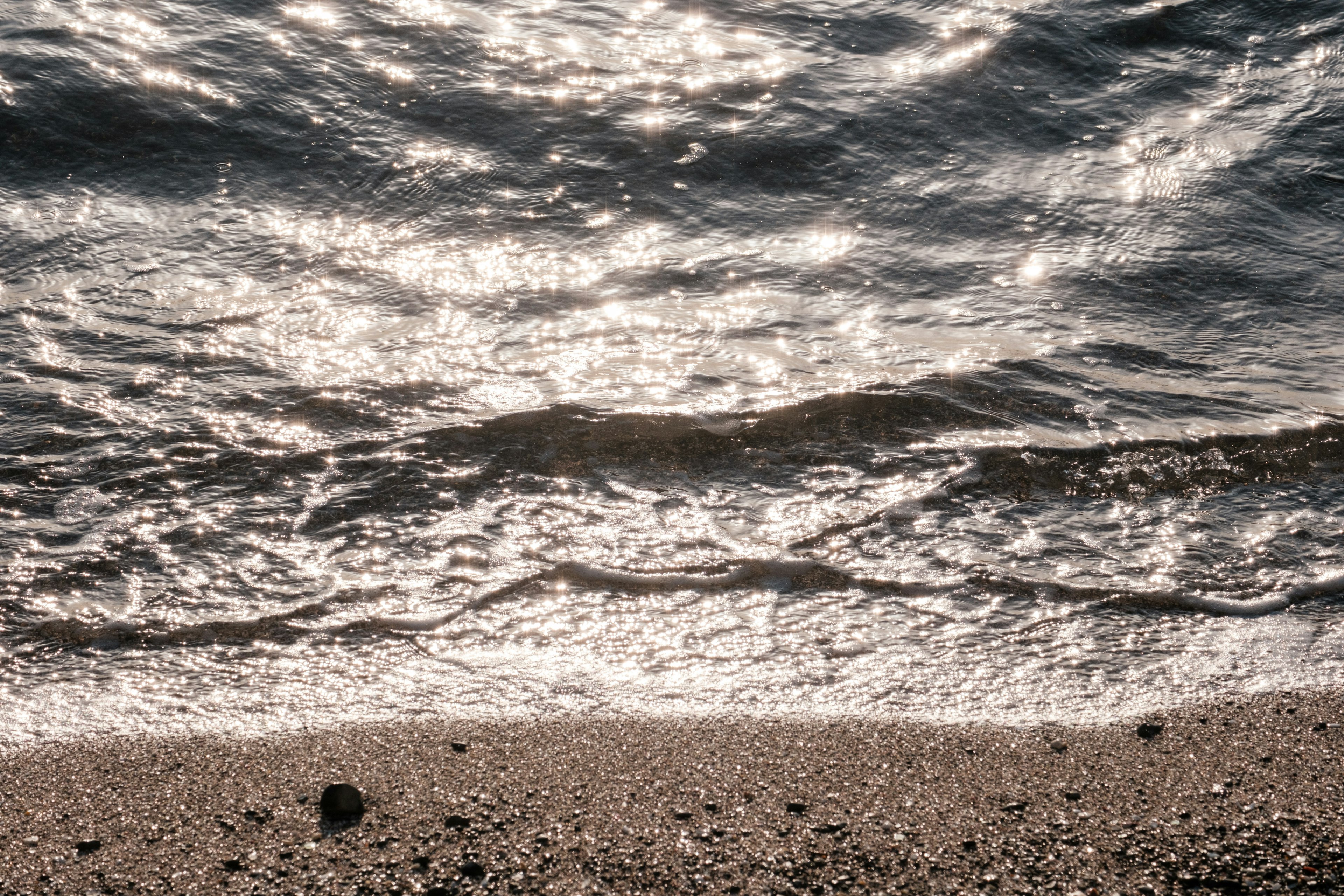 Nahaufnahme von schimmernden Wasserwellen und Sandstrand