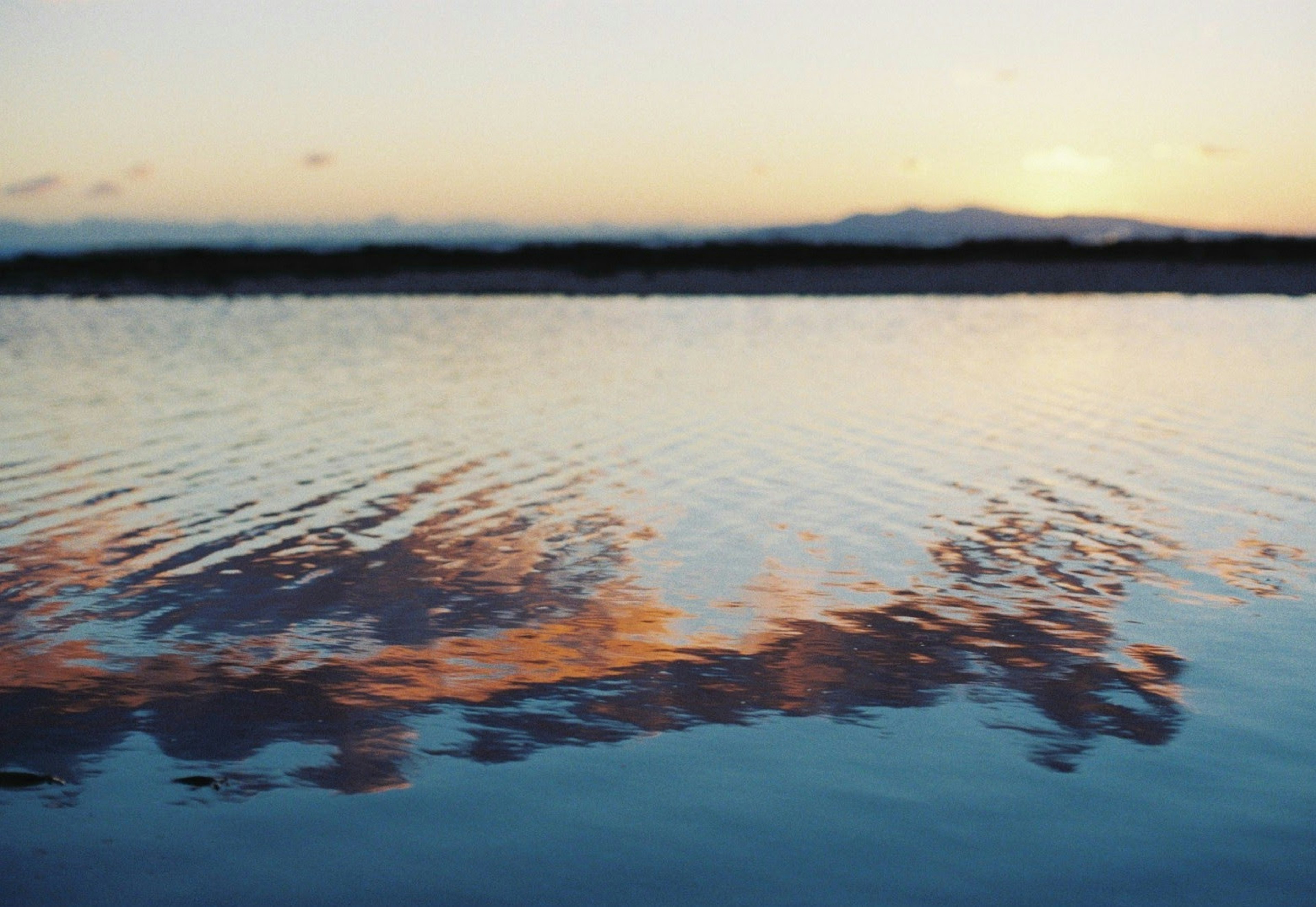 Surface d'eau sereine reflétant le coucher de soleil et les nuages