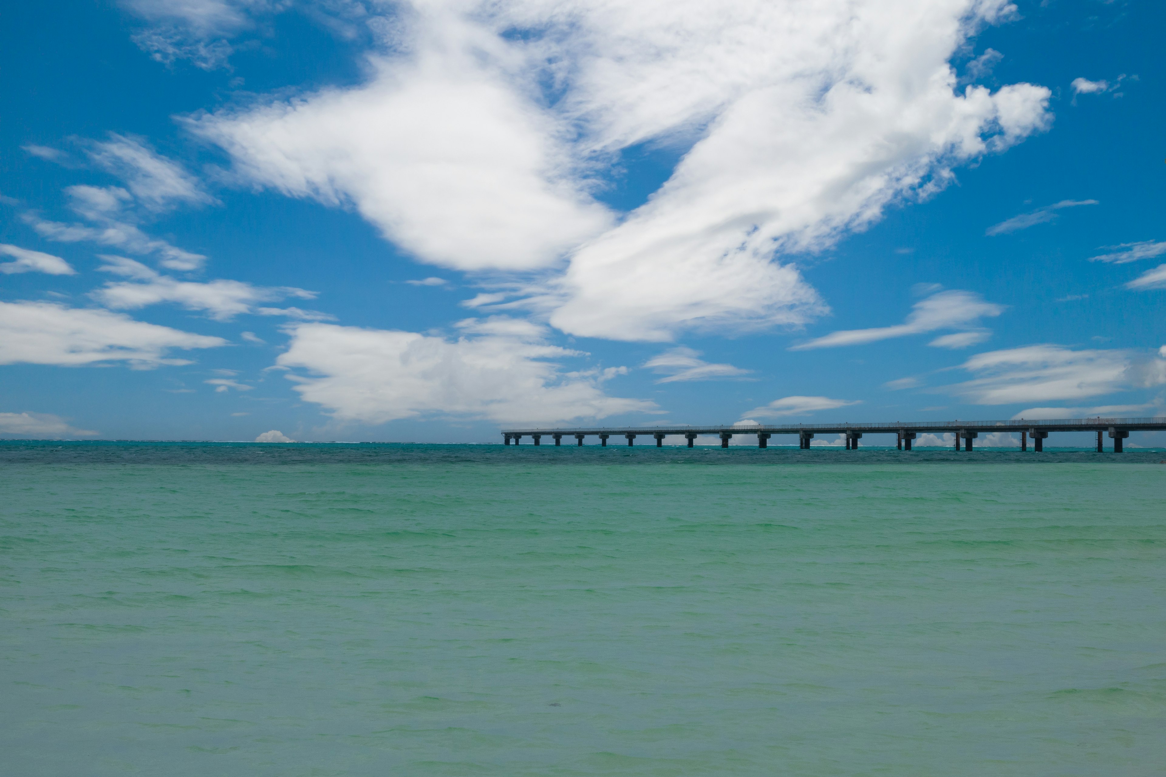 青い空と白い雲の下に広がる穏やかな海と桟橋