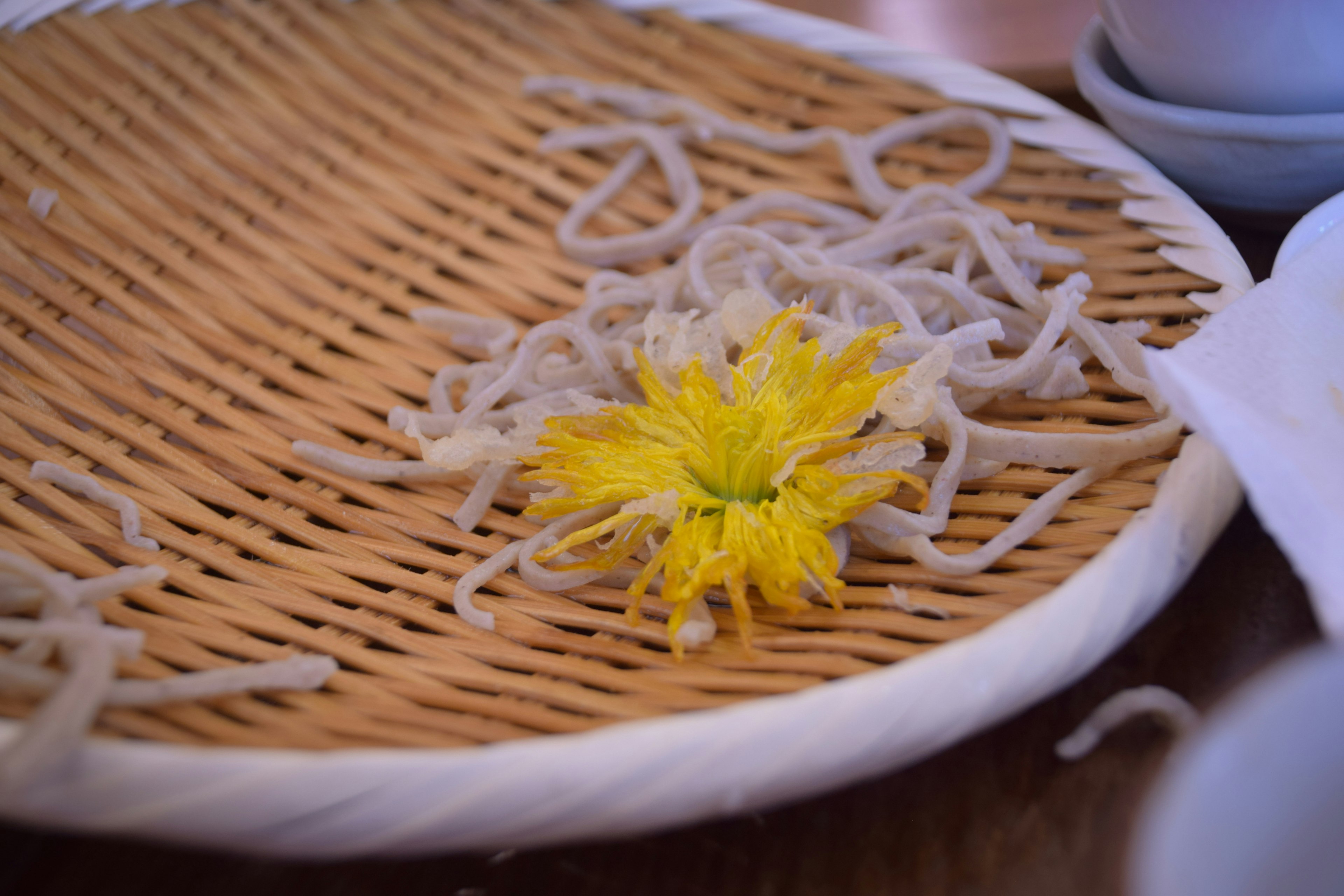 A bamboo plate with white noodles and a yellow flower