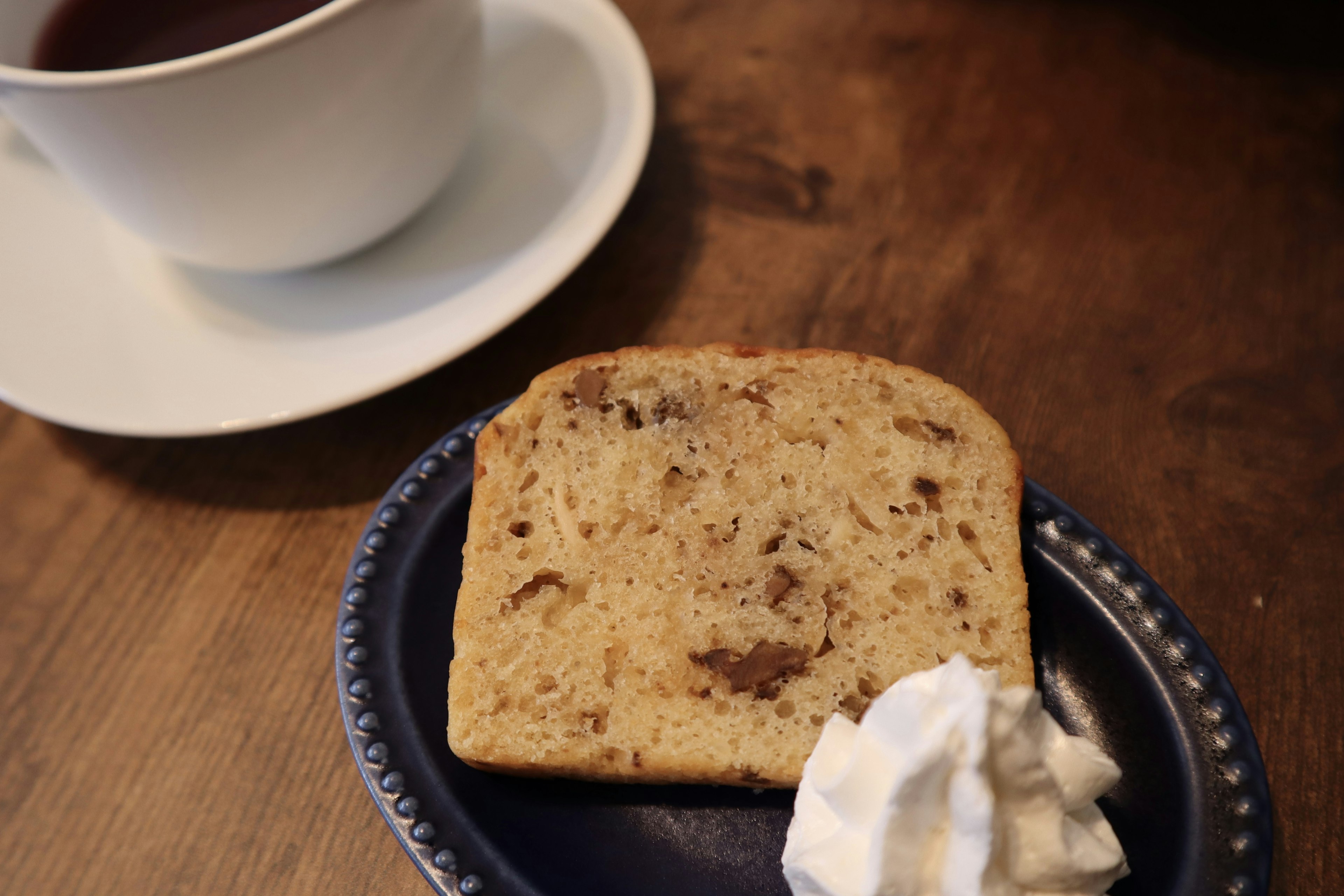 Ein Stück Kuchen mit Schlagsahne neben einer Tasse Kaffee auf einem Holztisch