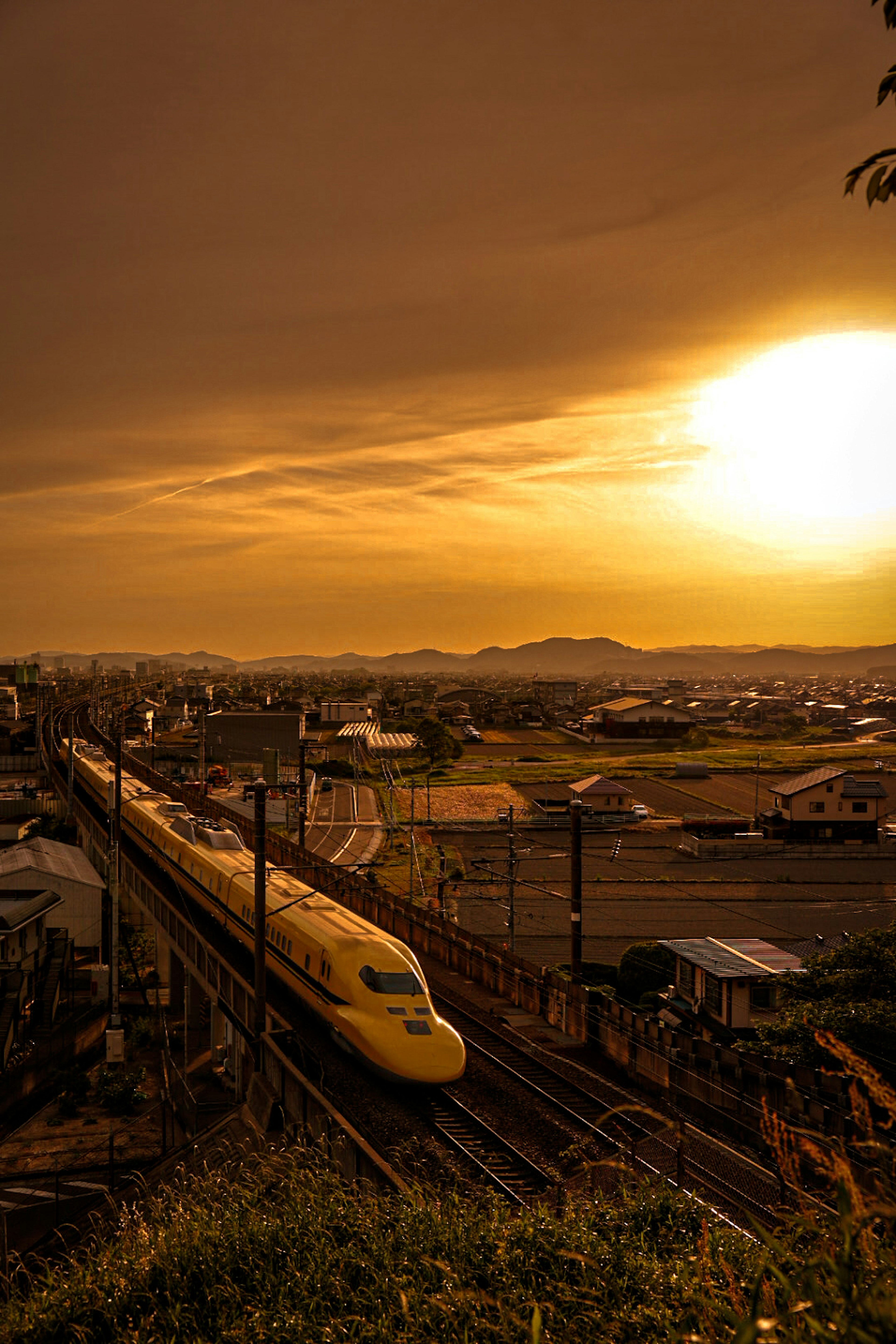 夕焼けの空を背景に走る黄色い新幹線