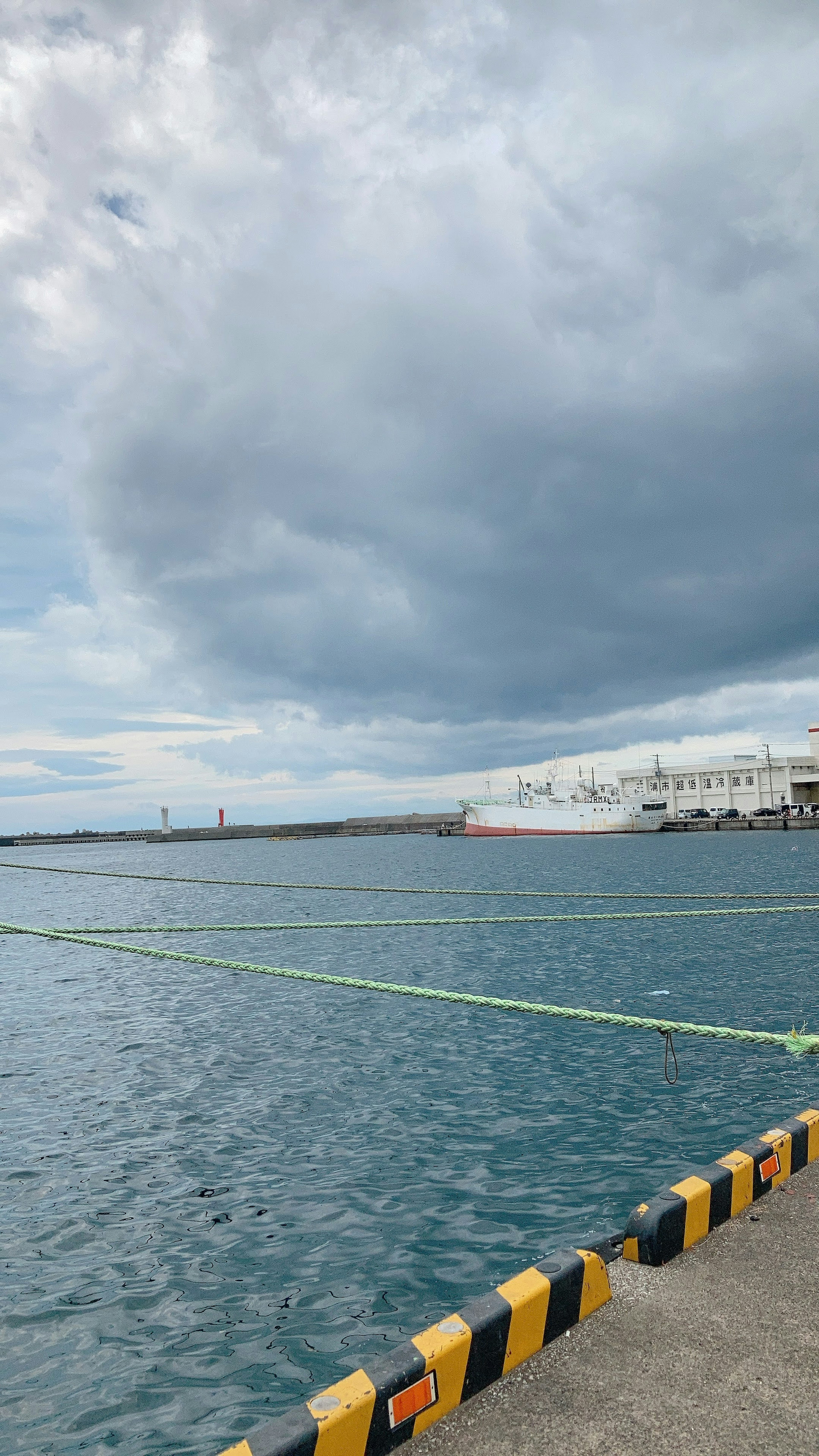 Welliger Ozean unter einem bewölkten Himmel mit einer gelb-schwarzen Barriere im Hafen