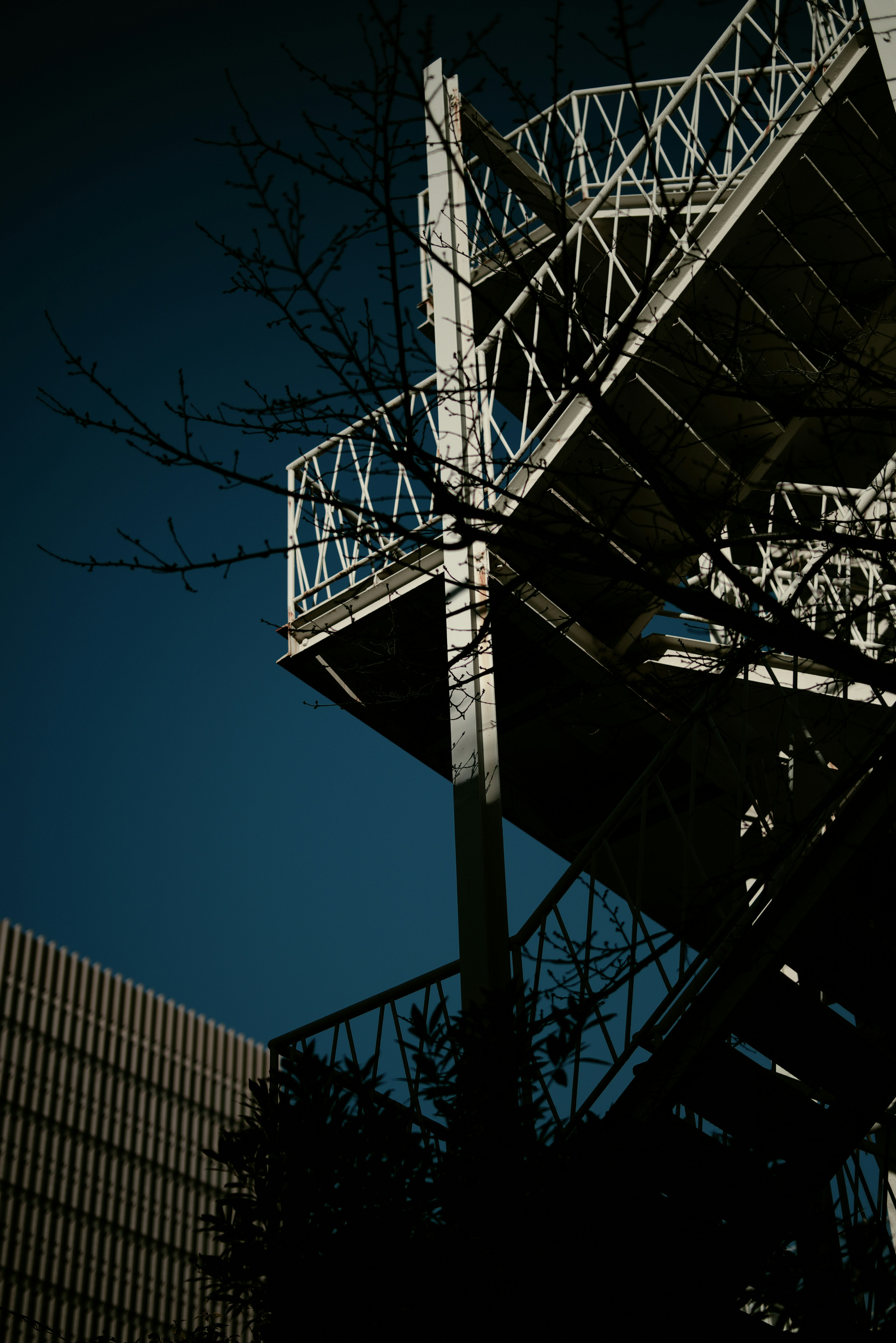 Escalera de metal bajo un cielo azul con siluetas de árboles