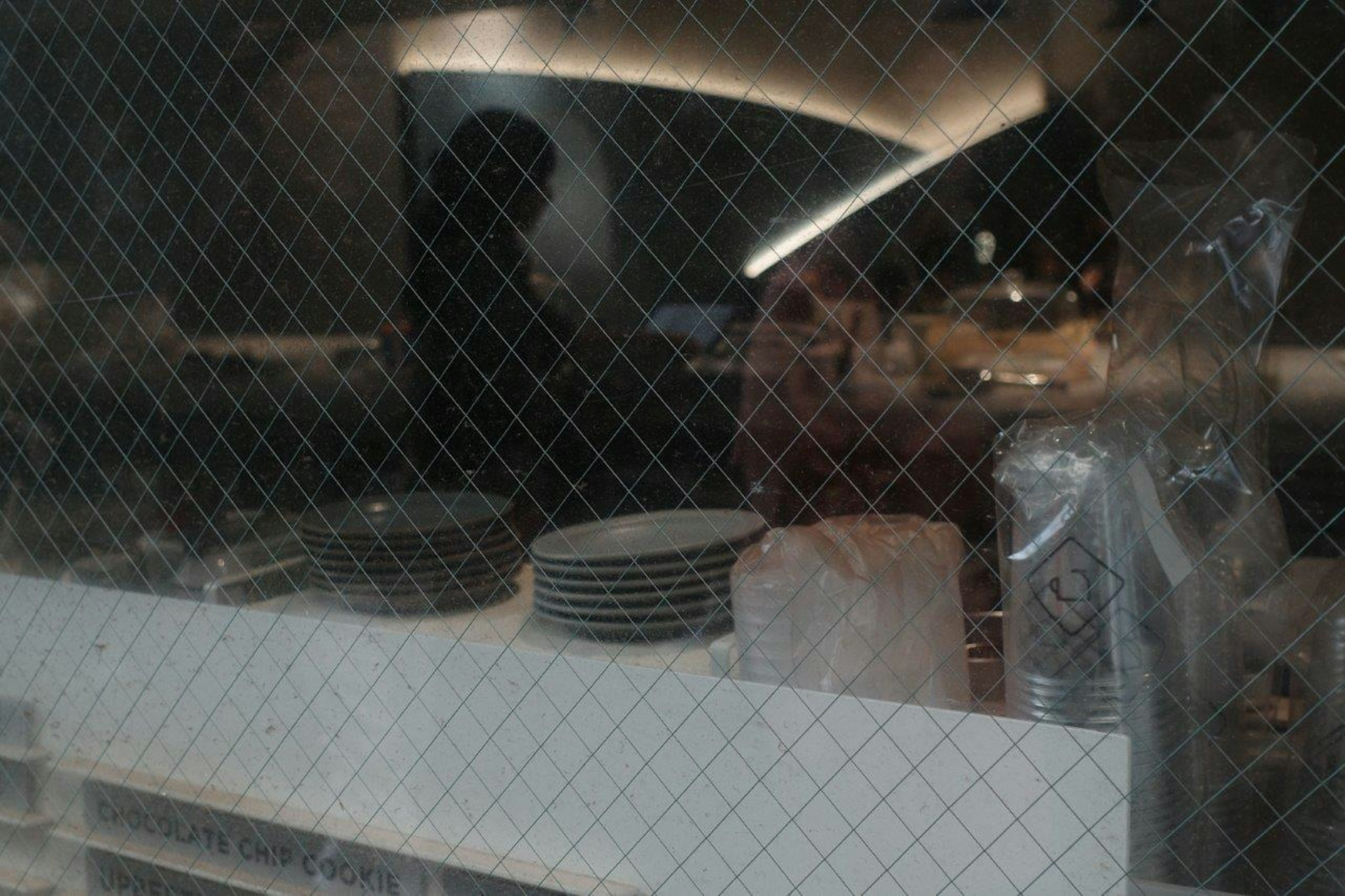 View of a restaurant kitchen through a window with plates and cooking utensils visible