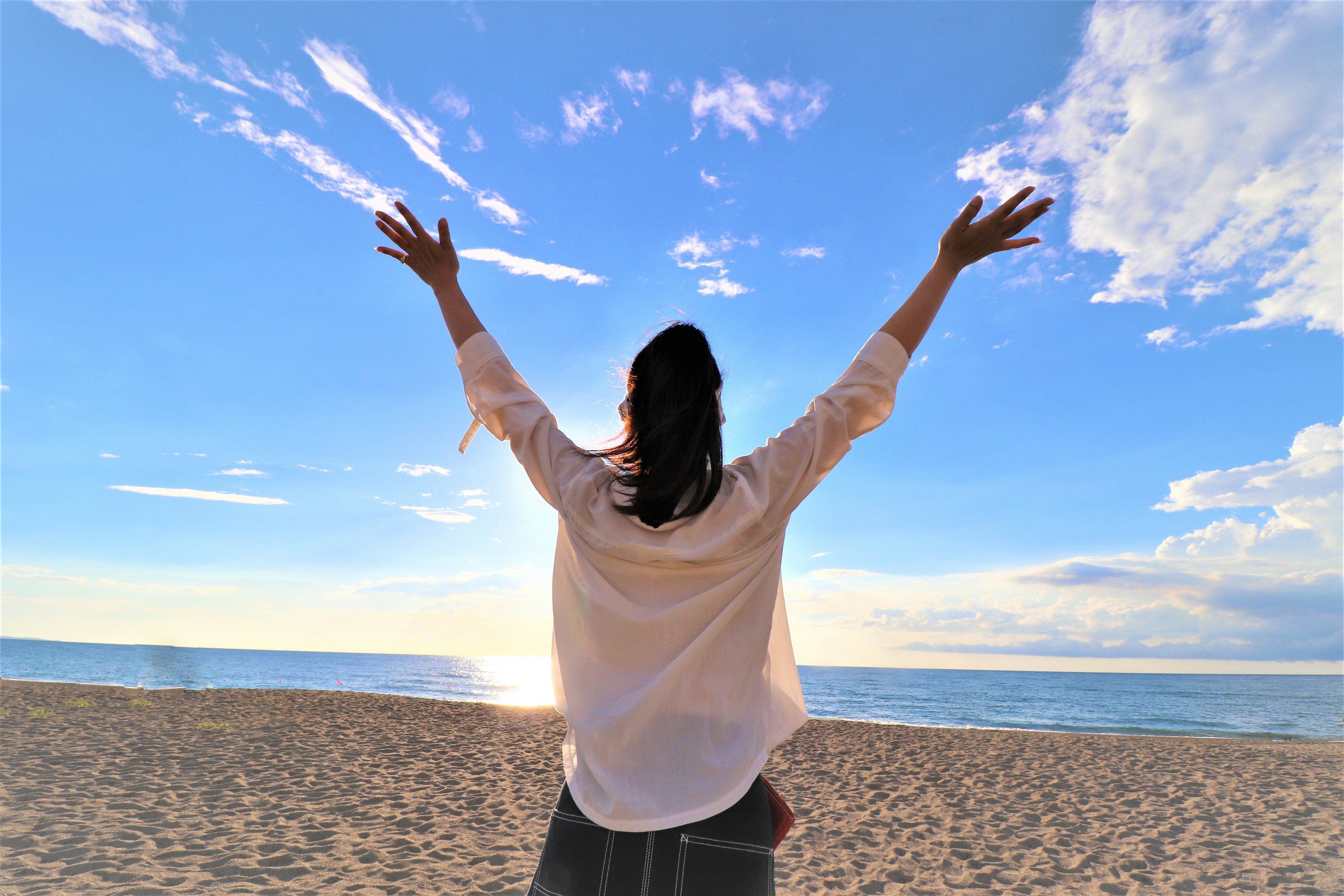 Une femme les bras écartés sur la plage sous un ciel bleu et des nuages