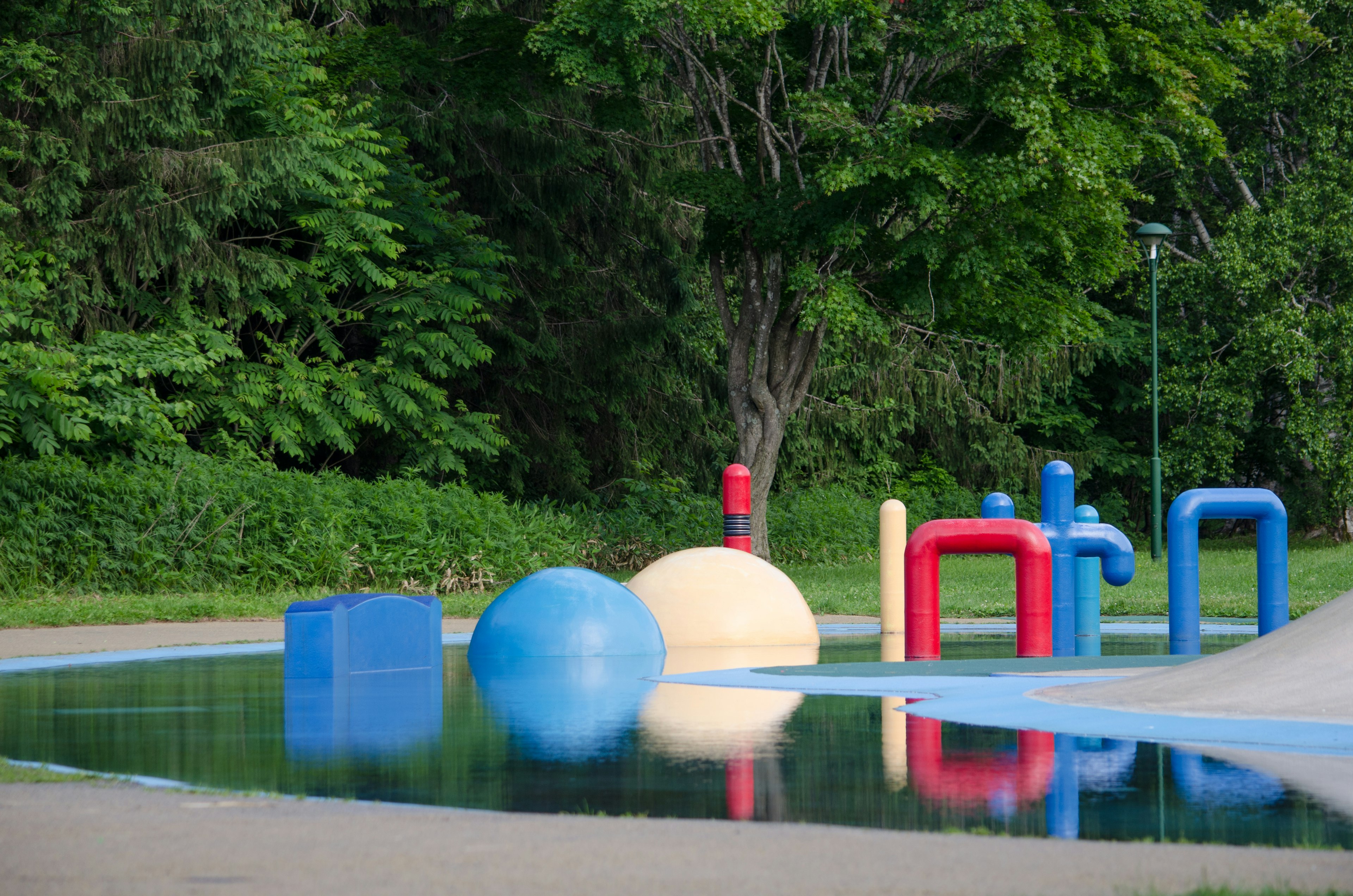 Buntes Spielplatzgerät neben einer reflektierenden Wasseroberfläche in einem Park