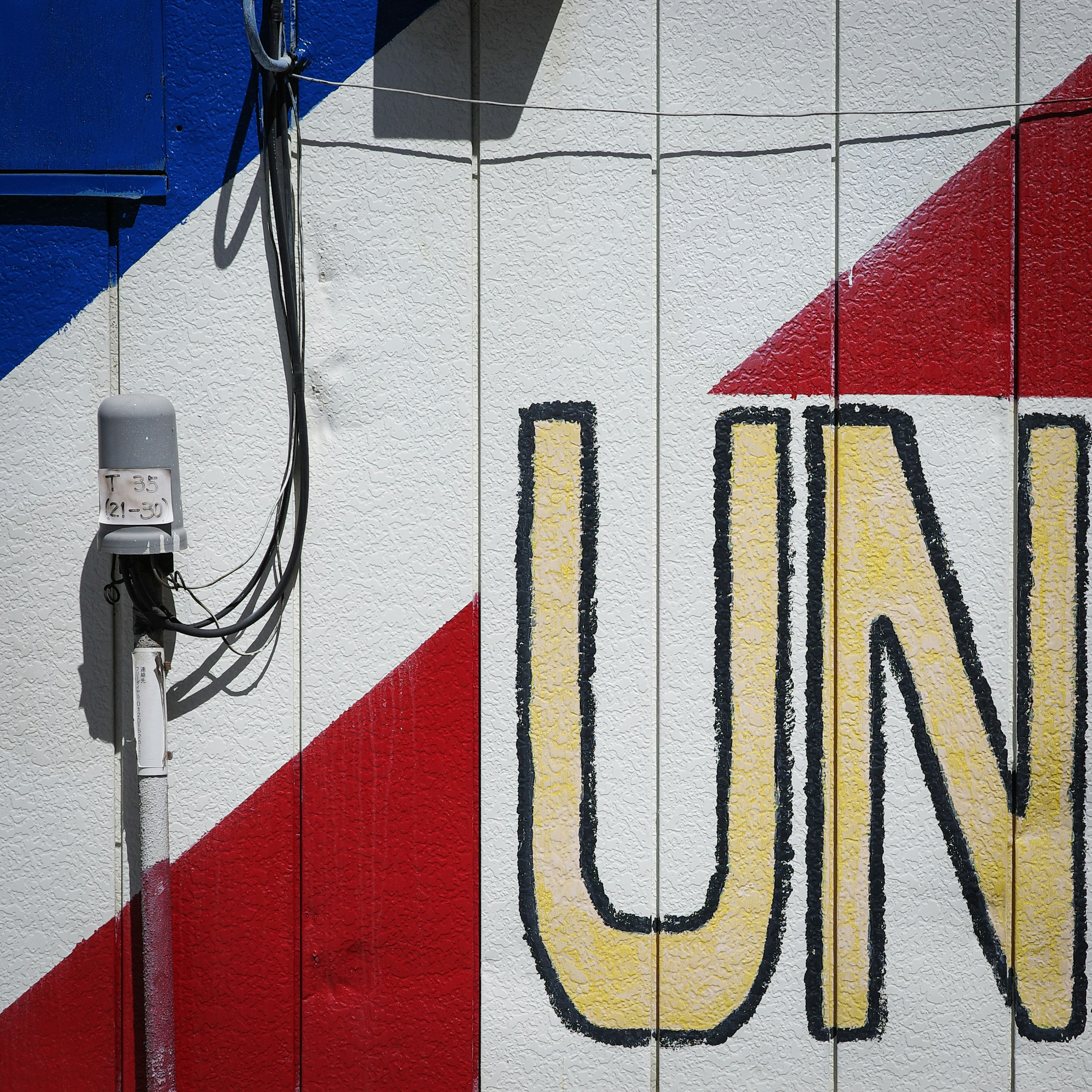 Teil einer Wand mit roten und blauen Streifen, die große gelbe Buchstaben mit 'UN' zeigt