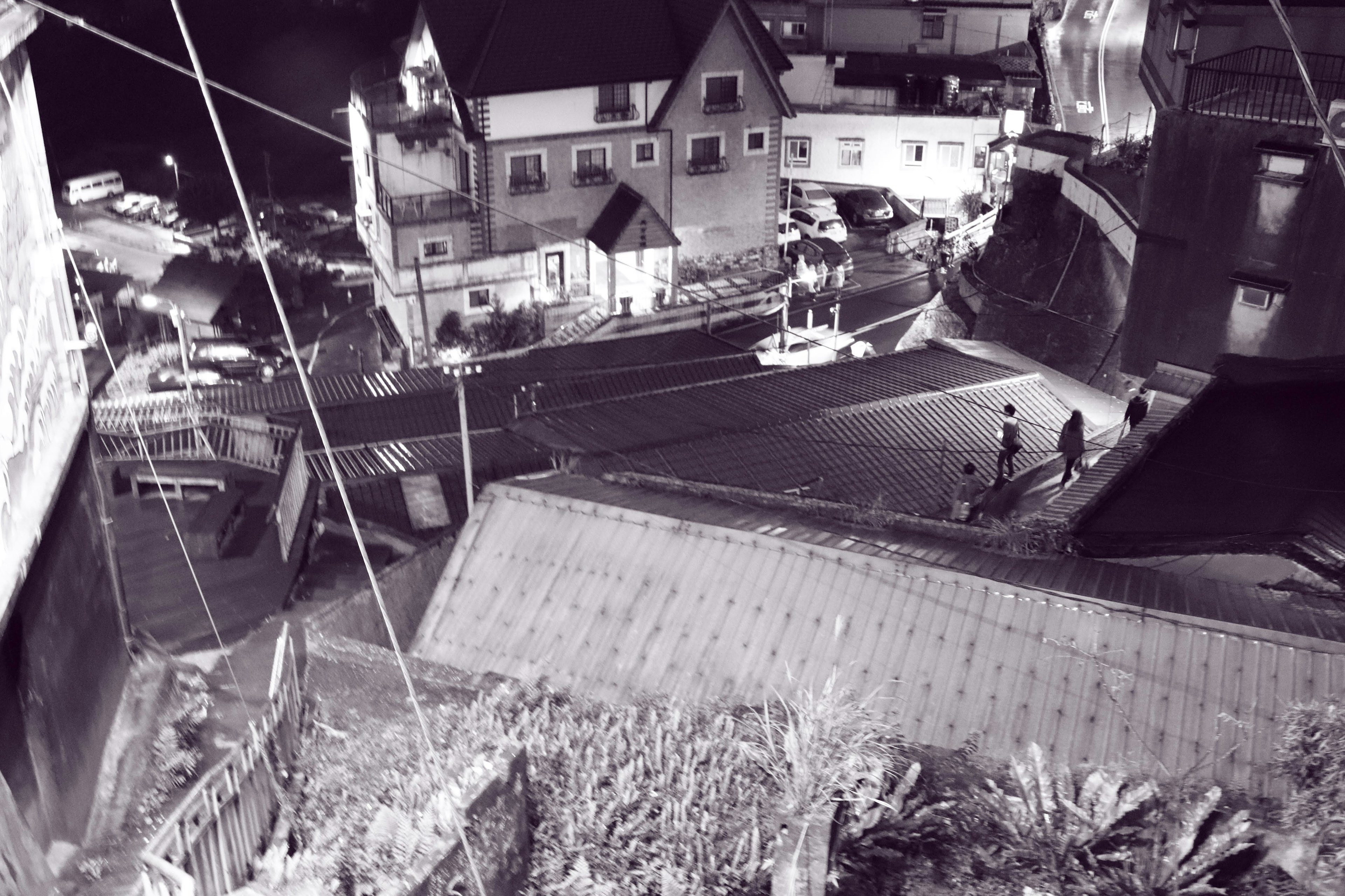 Paysage urbain en noir et blanc montrant des maisons et des routes avec des personnes marchant à proximité