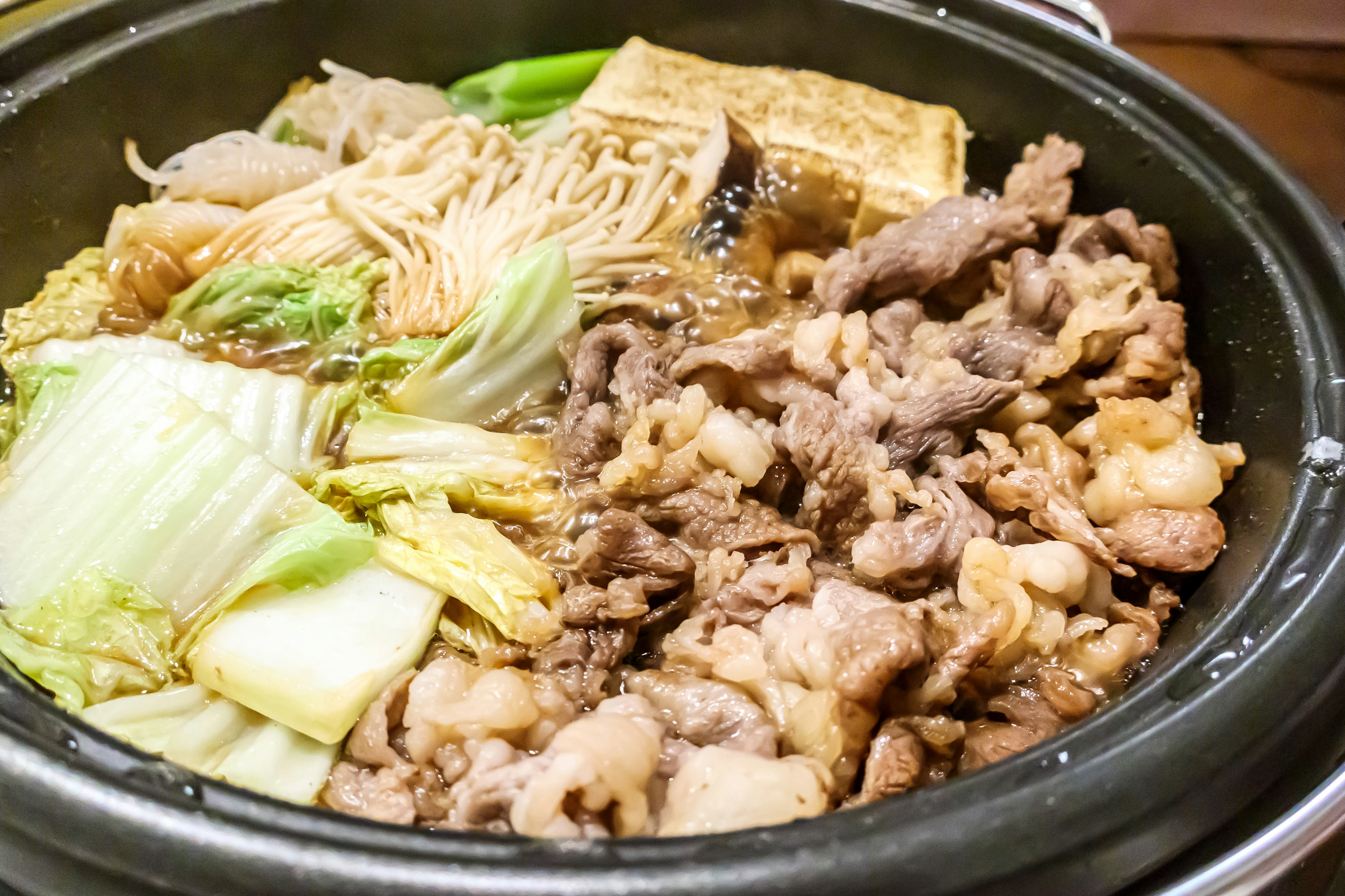 A pot of hot pot featuring various meats, vegetables, tofu, and noodles