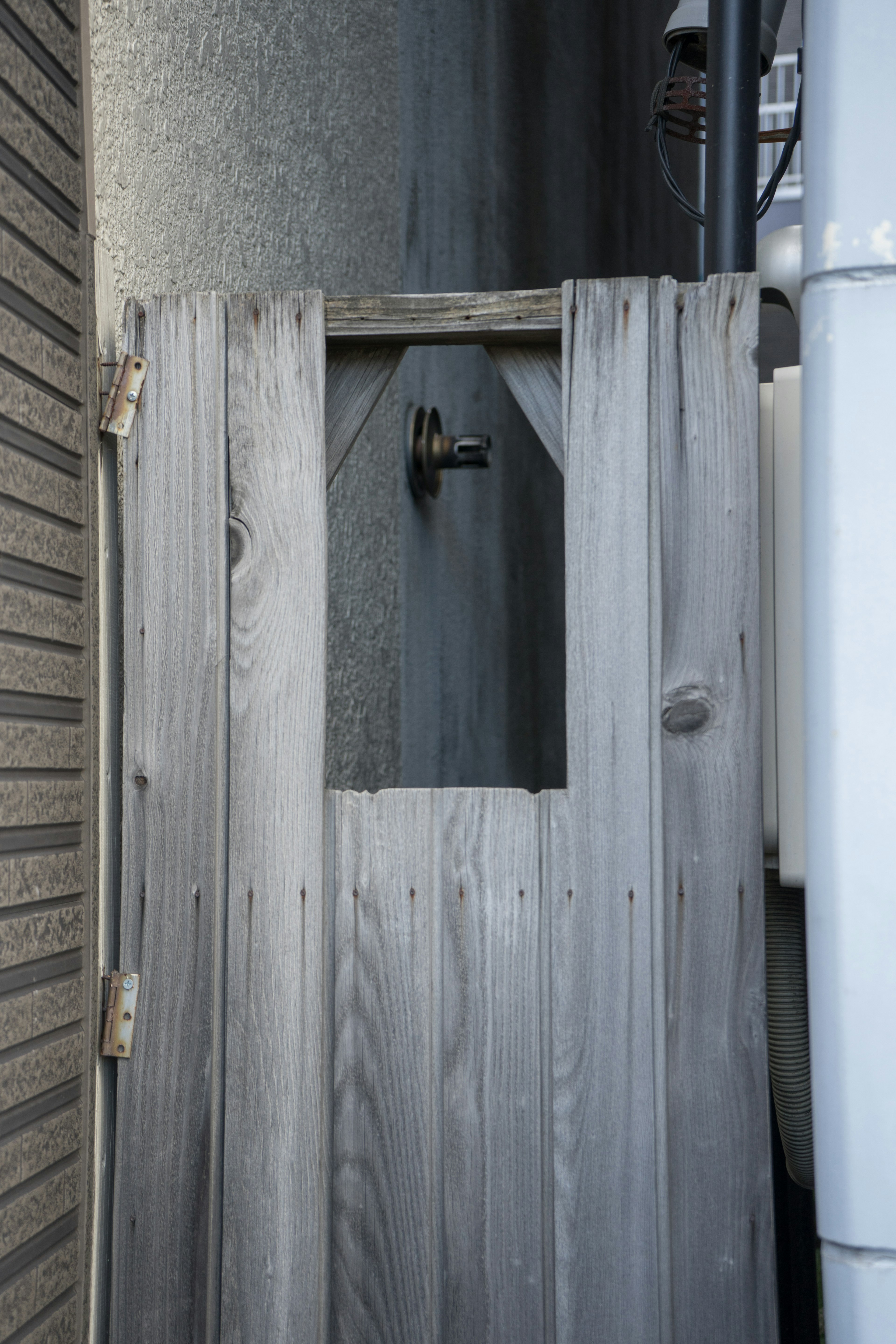 A gap in a wooden fence revealing a metal pipe