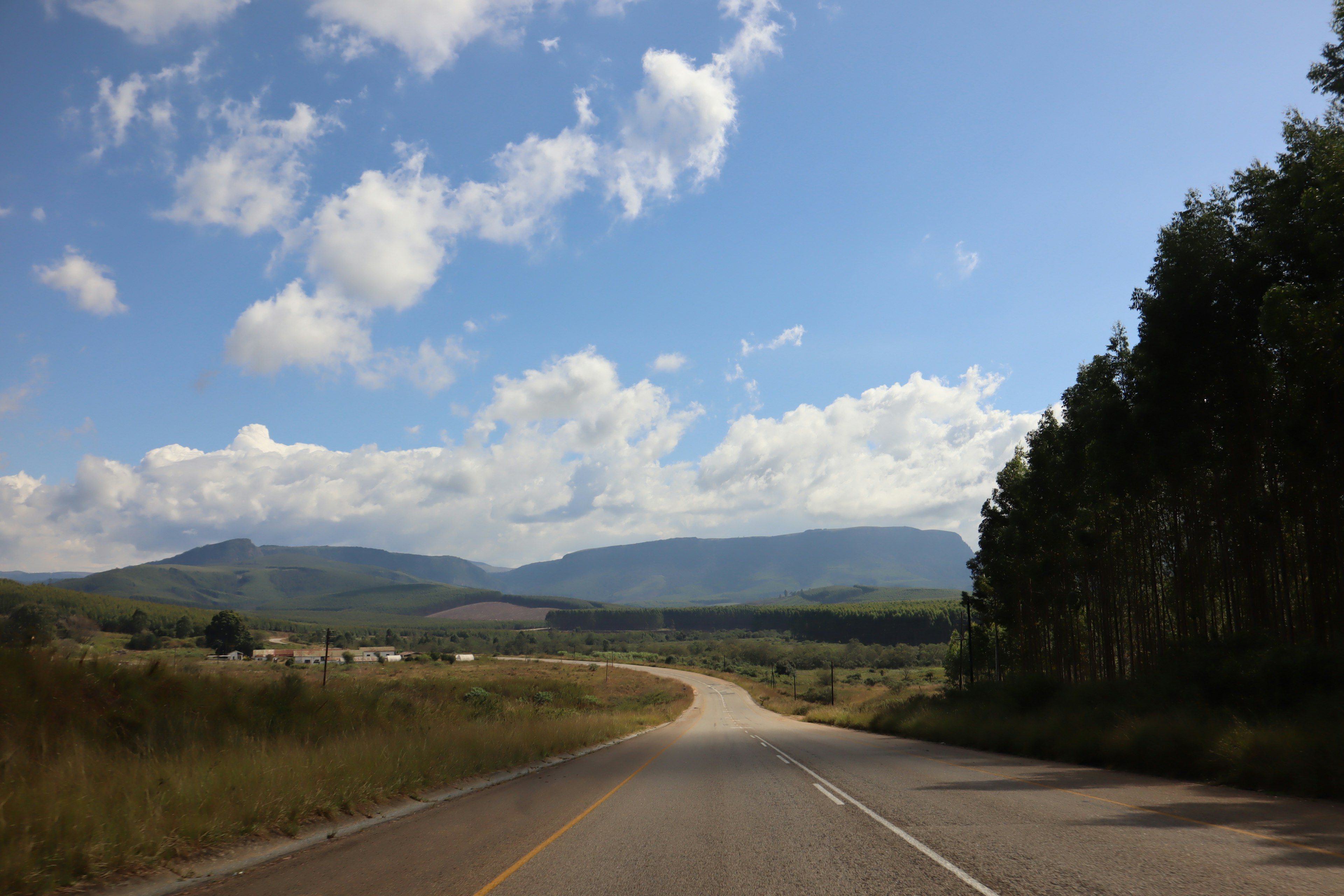 Curving road with mountains under a blue sky and white clouds