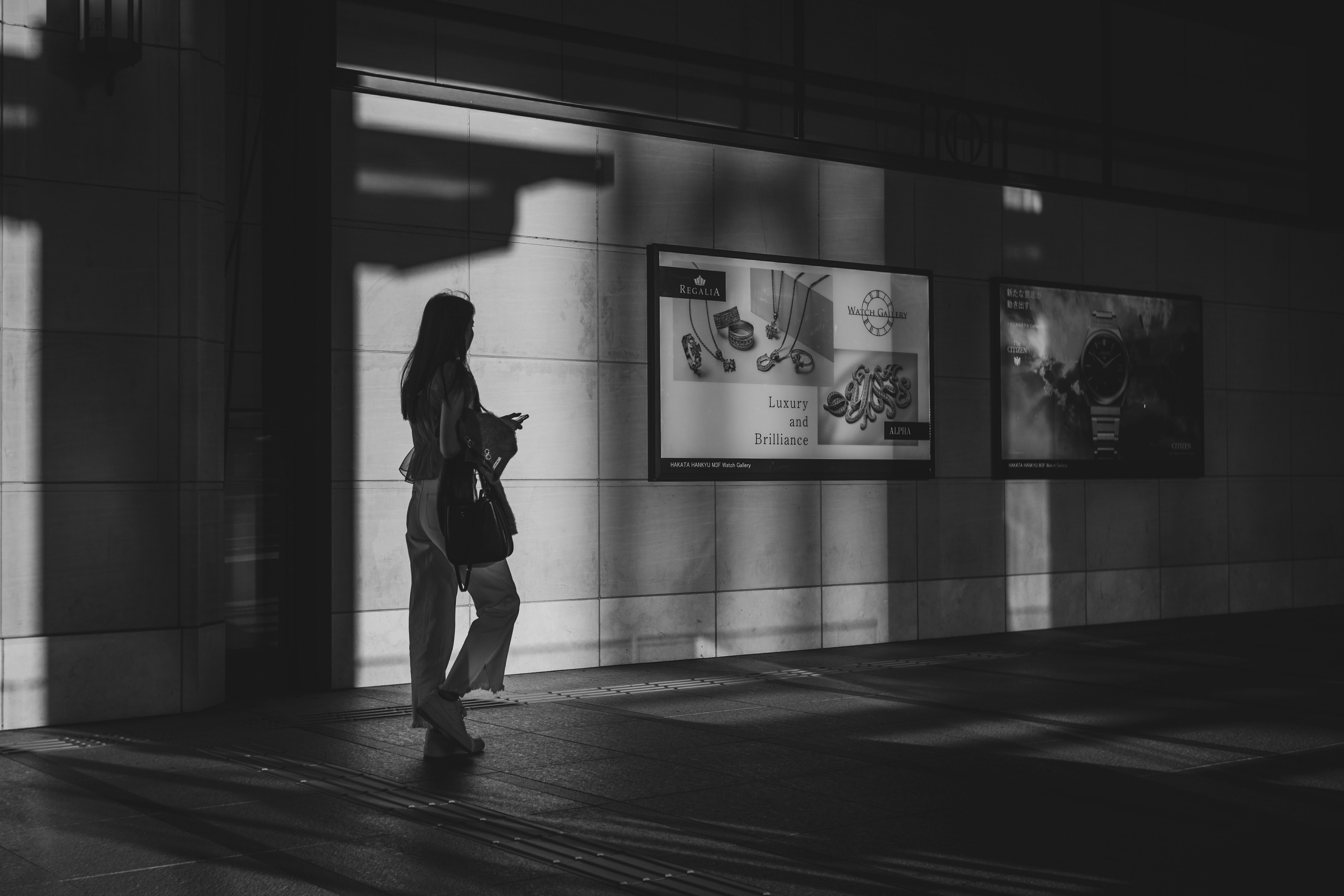 Une femme marchant dans l'ombre photo en noir et blanc avec des publicités sur le mur