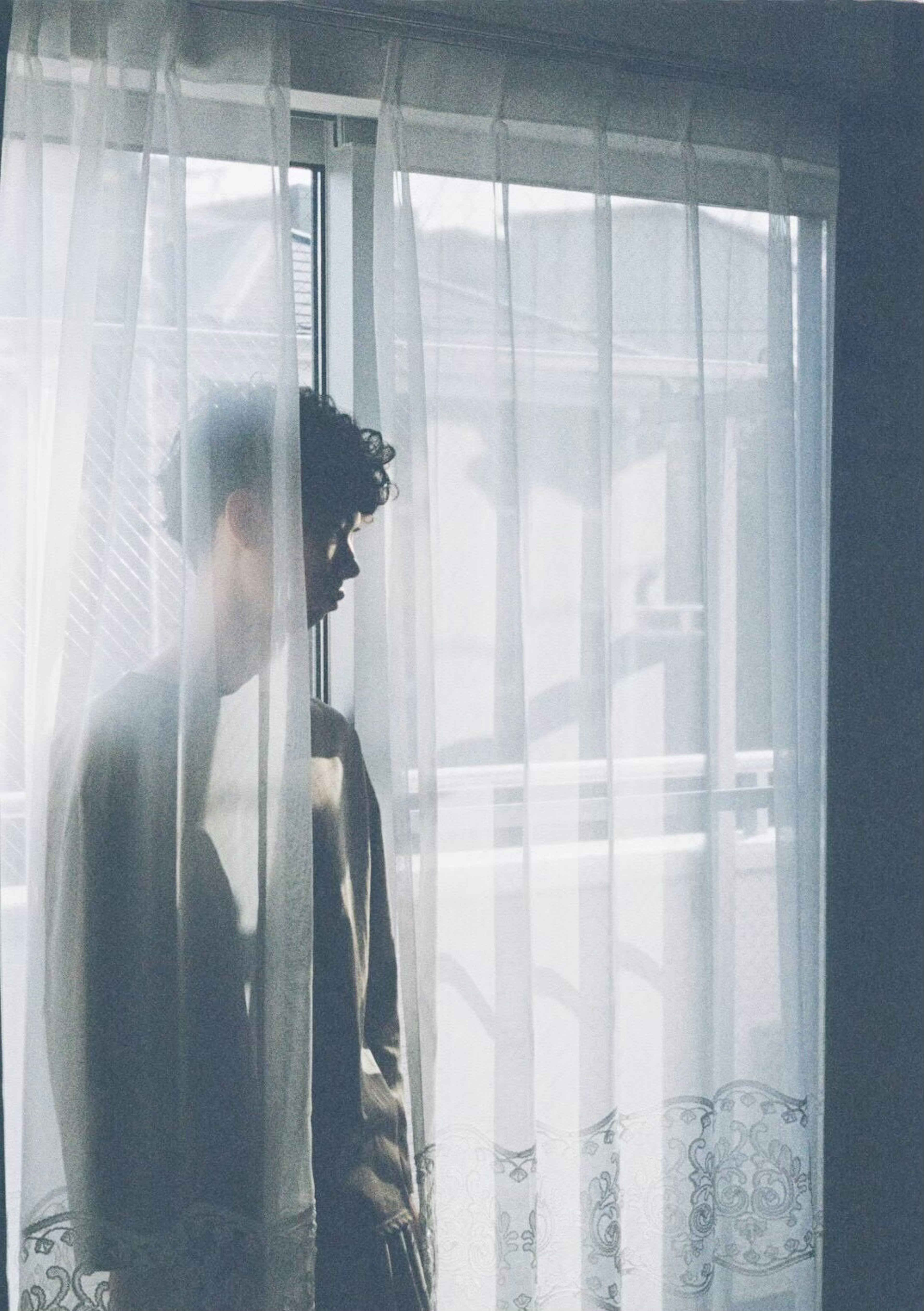 Silhouette of a person standing behind sheer curtains Soft light filtering through