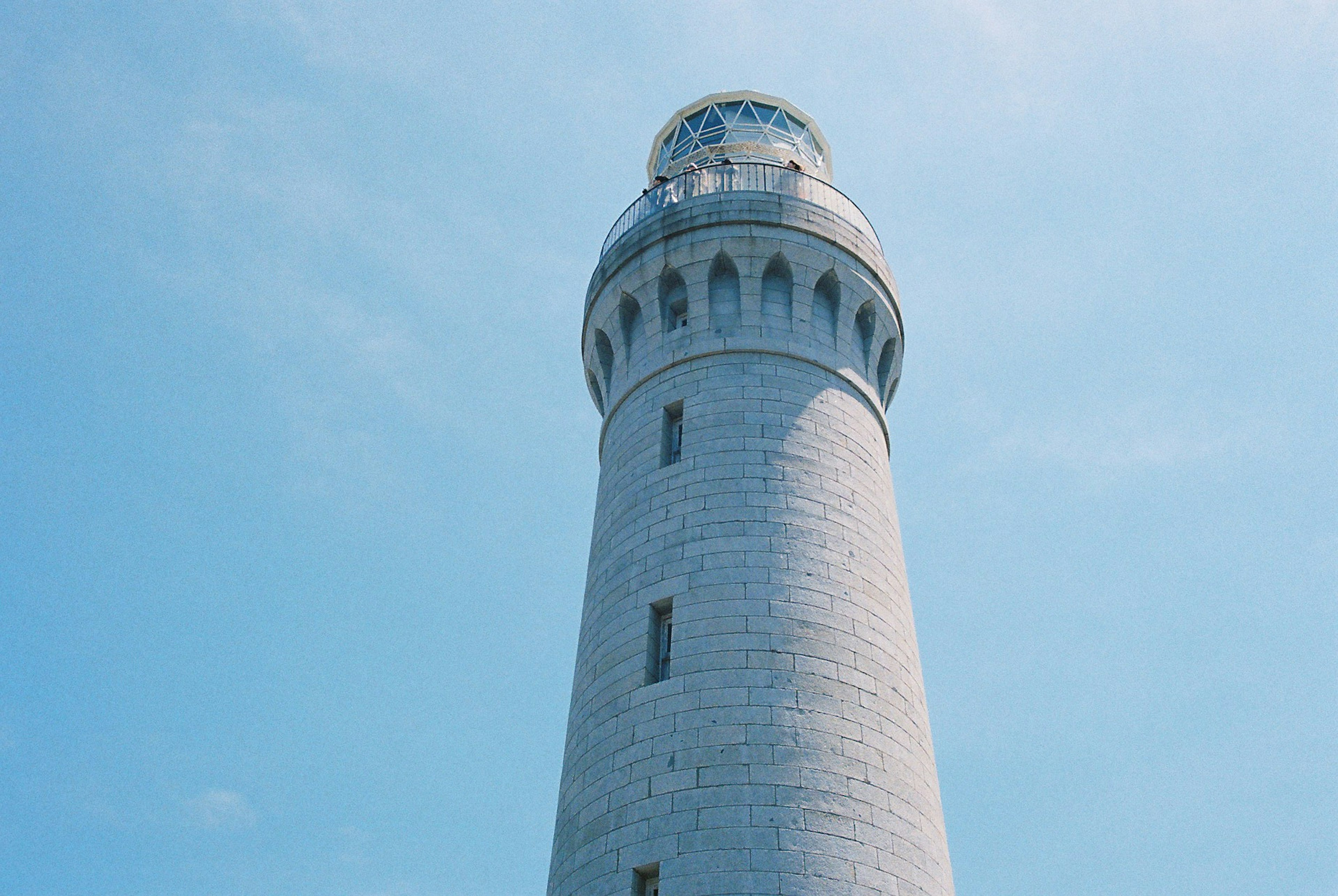 Primo piano di un faro bianco sotto un cielo blu chiaro