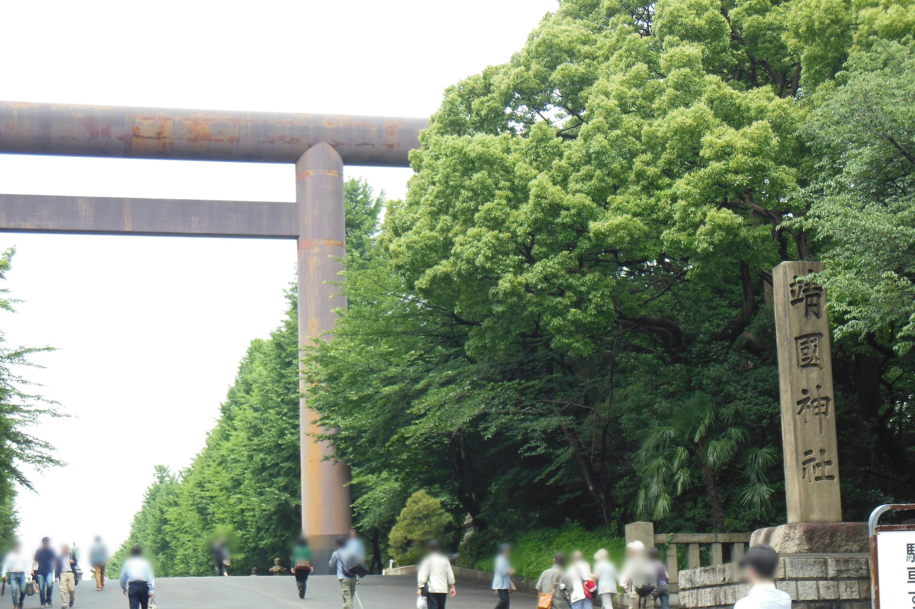 Ein Gehweg mit großen Eisenkonstruktionen und einem Steindenkmal, umgeben von grünen Bäumen