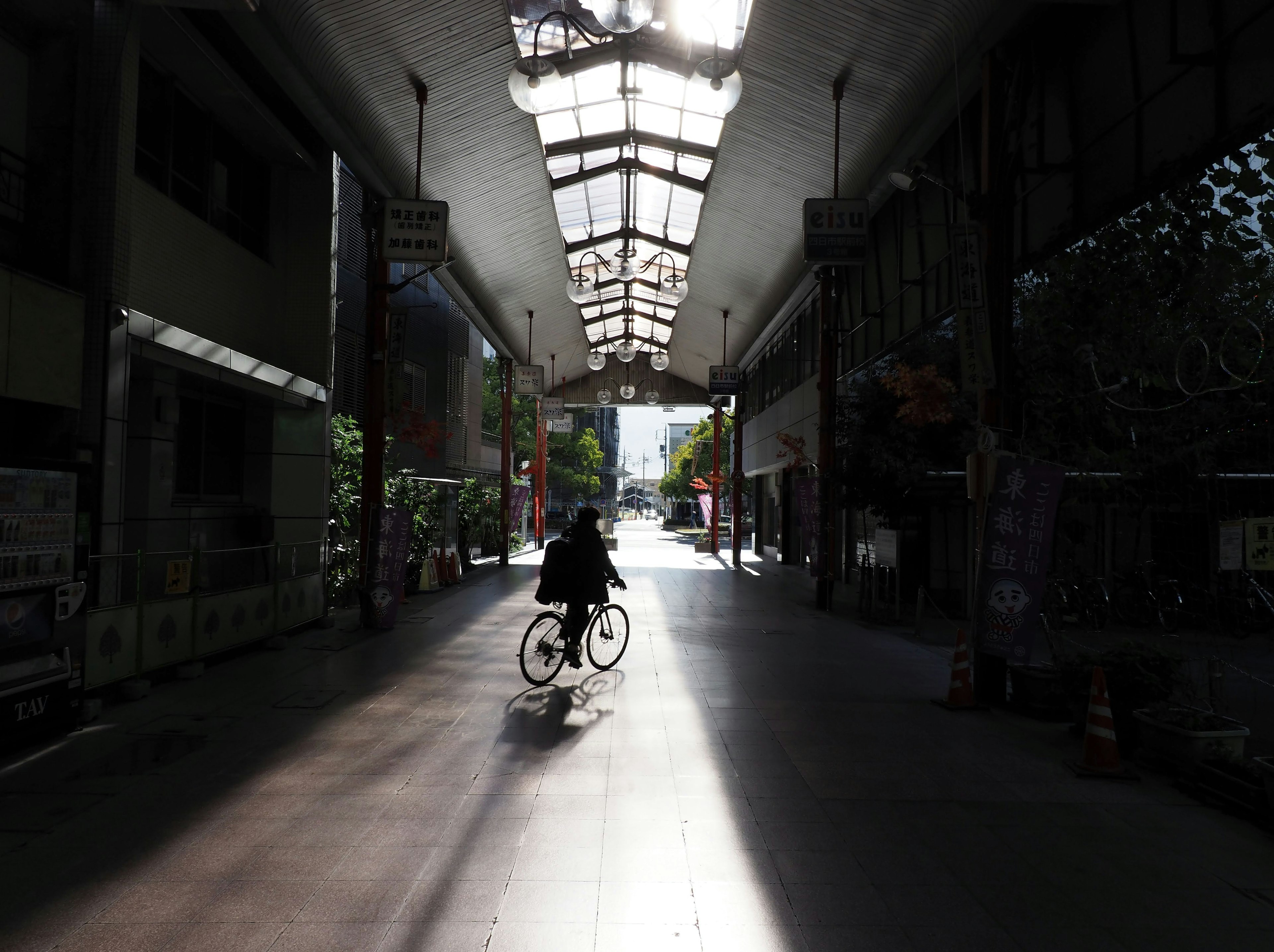 Une personne à vélo traversant une arcade commerçante calme avec la lumière du soleil créant de longues ombres