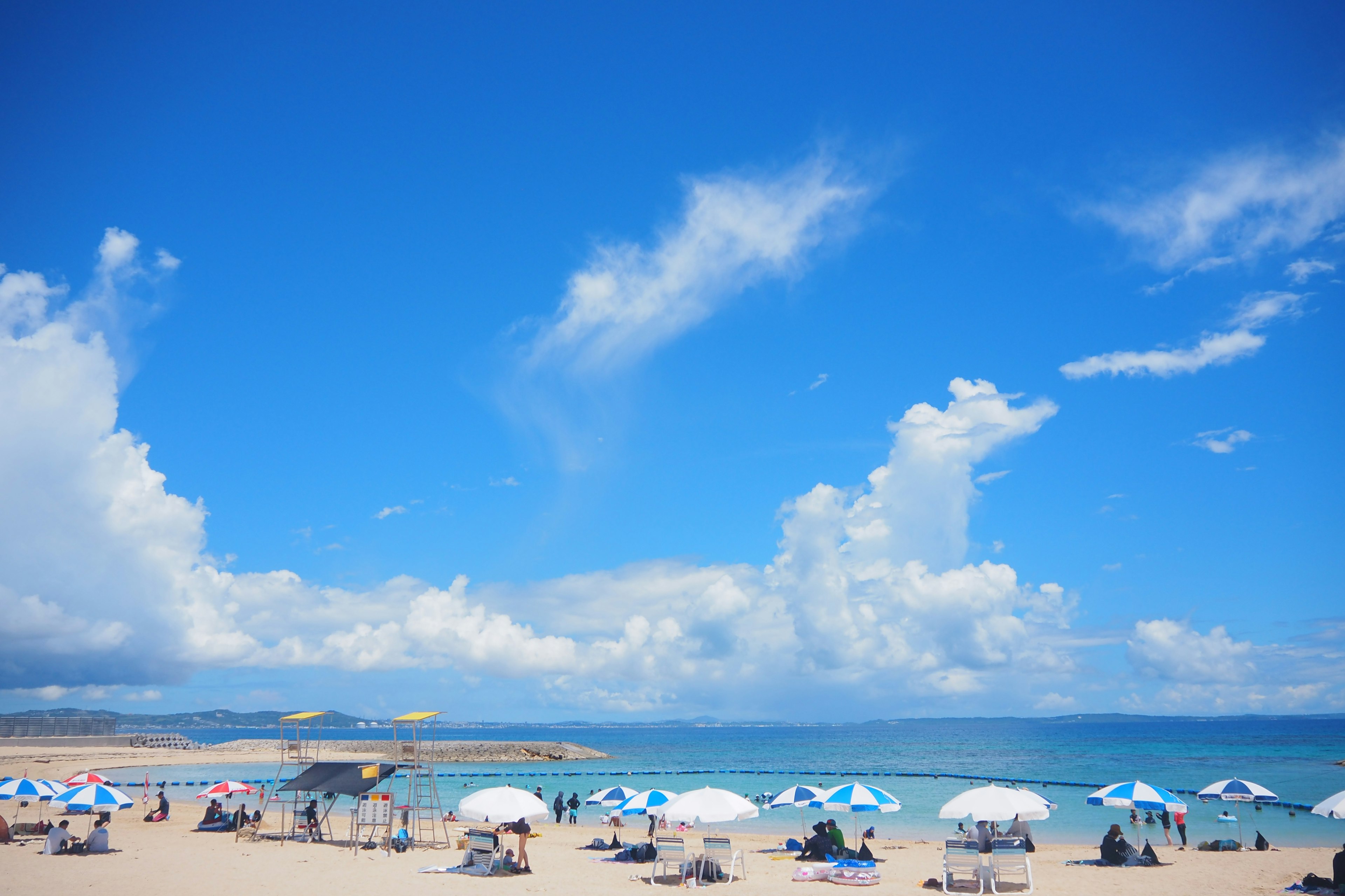 Pemandangan pantai dengan payung di bawah langit biru dan awan putih