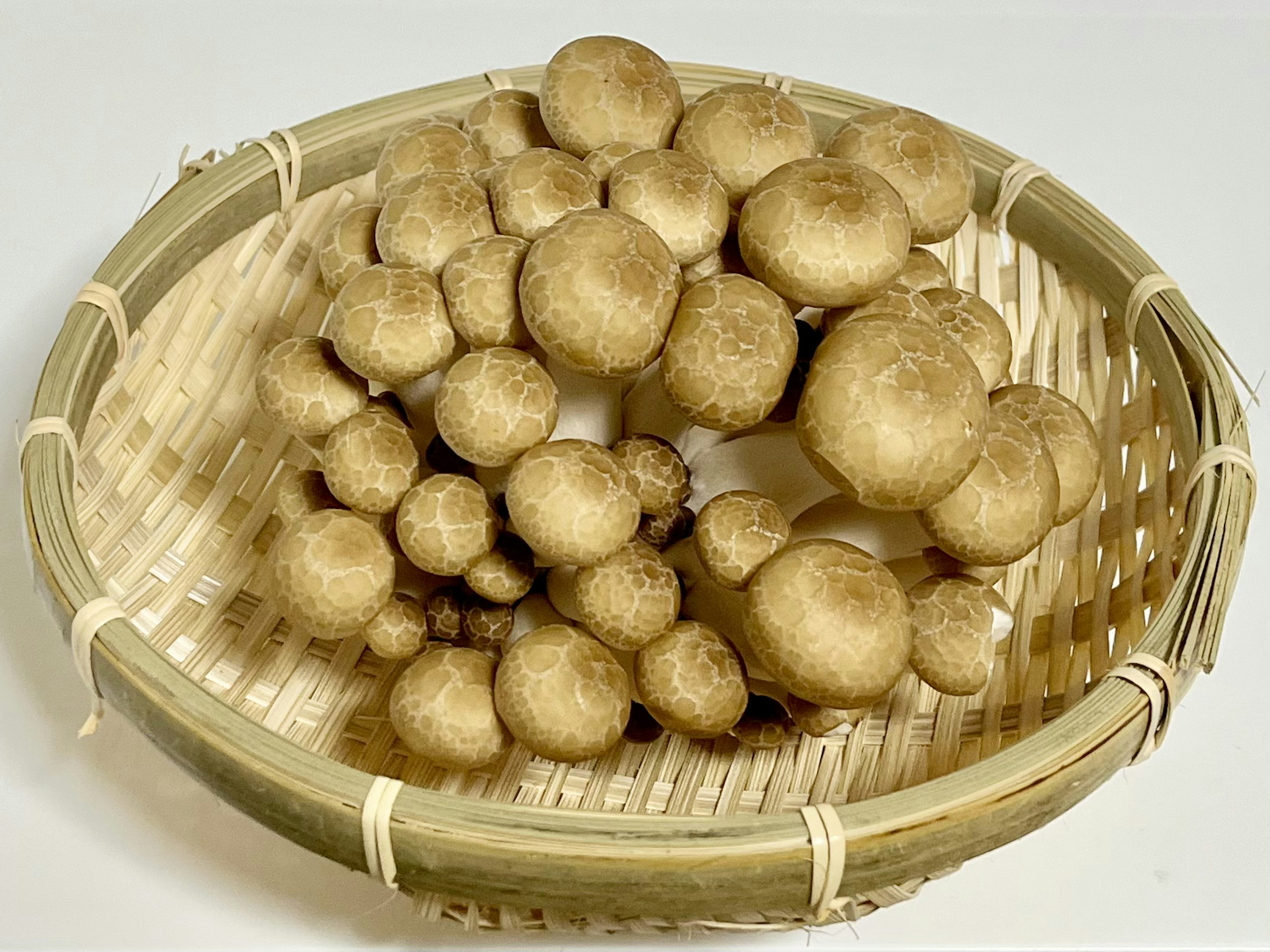 A large cluster of brown mushrooms arranged in a woven bamboo basket