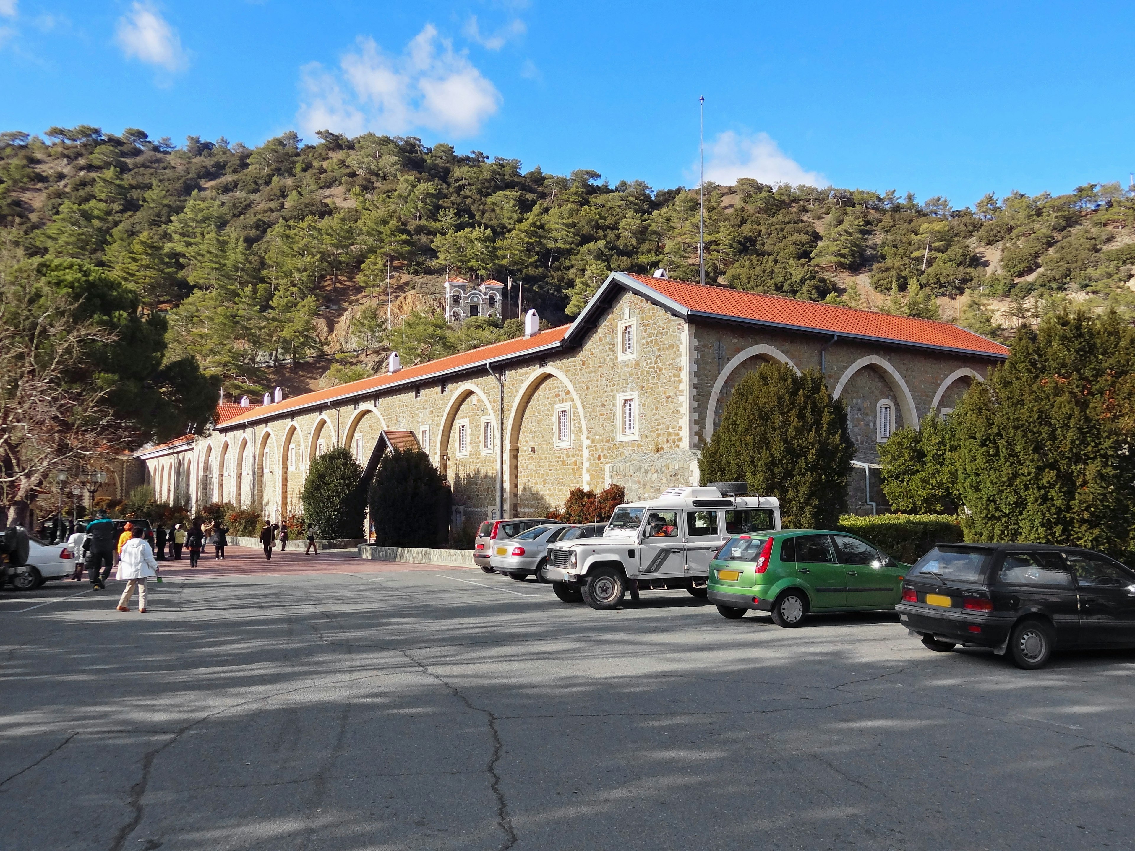 Stone building with arched windows surrounded by trees parking lot with cars