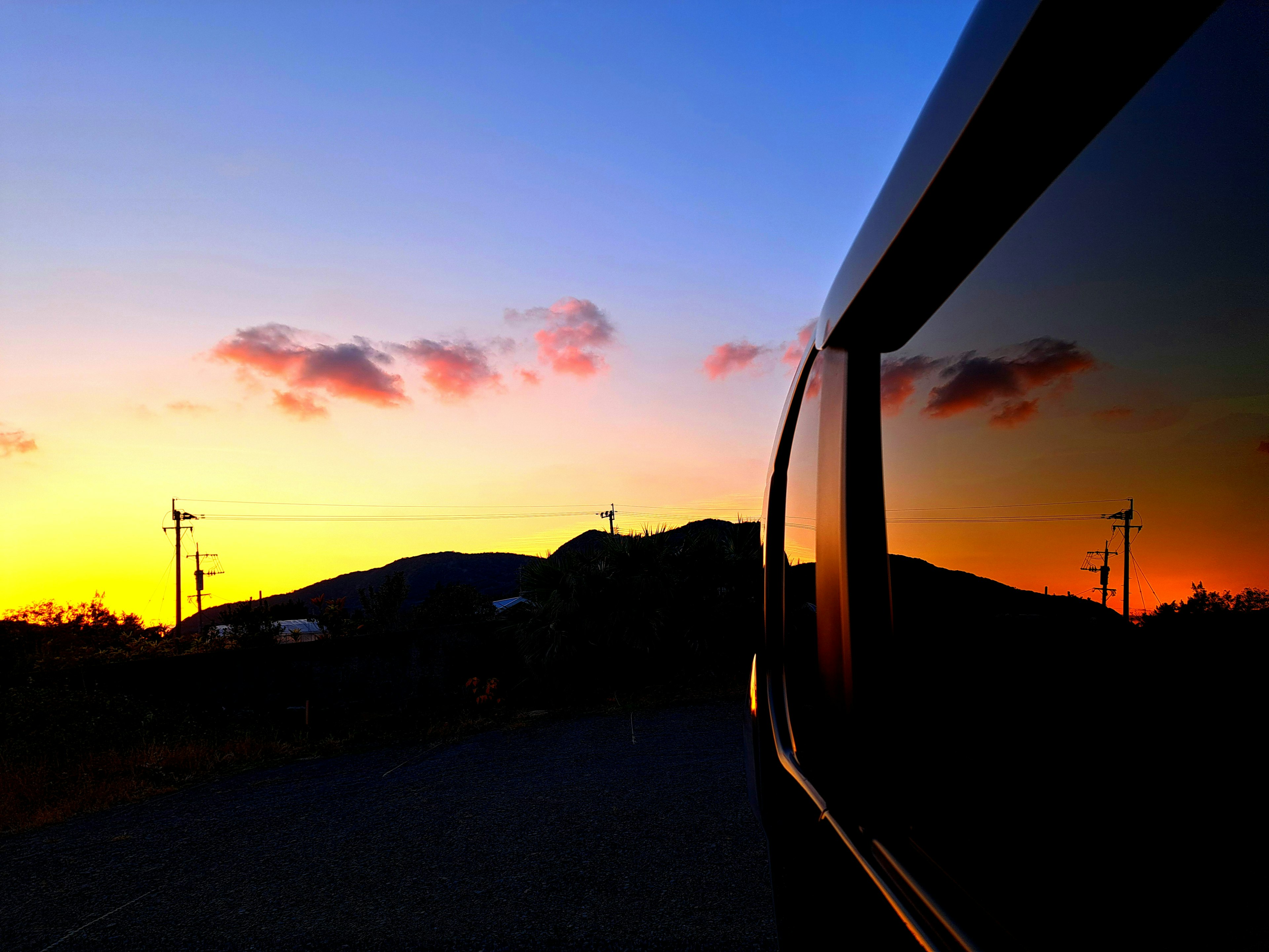 夕焼けの空と山の反射が映る車の窓