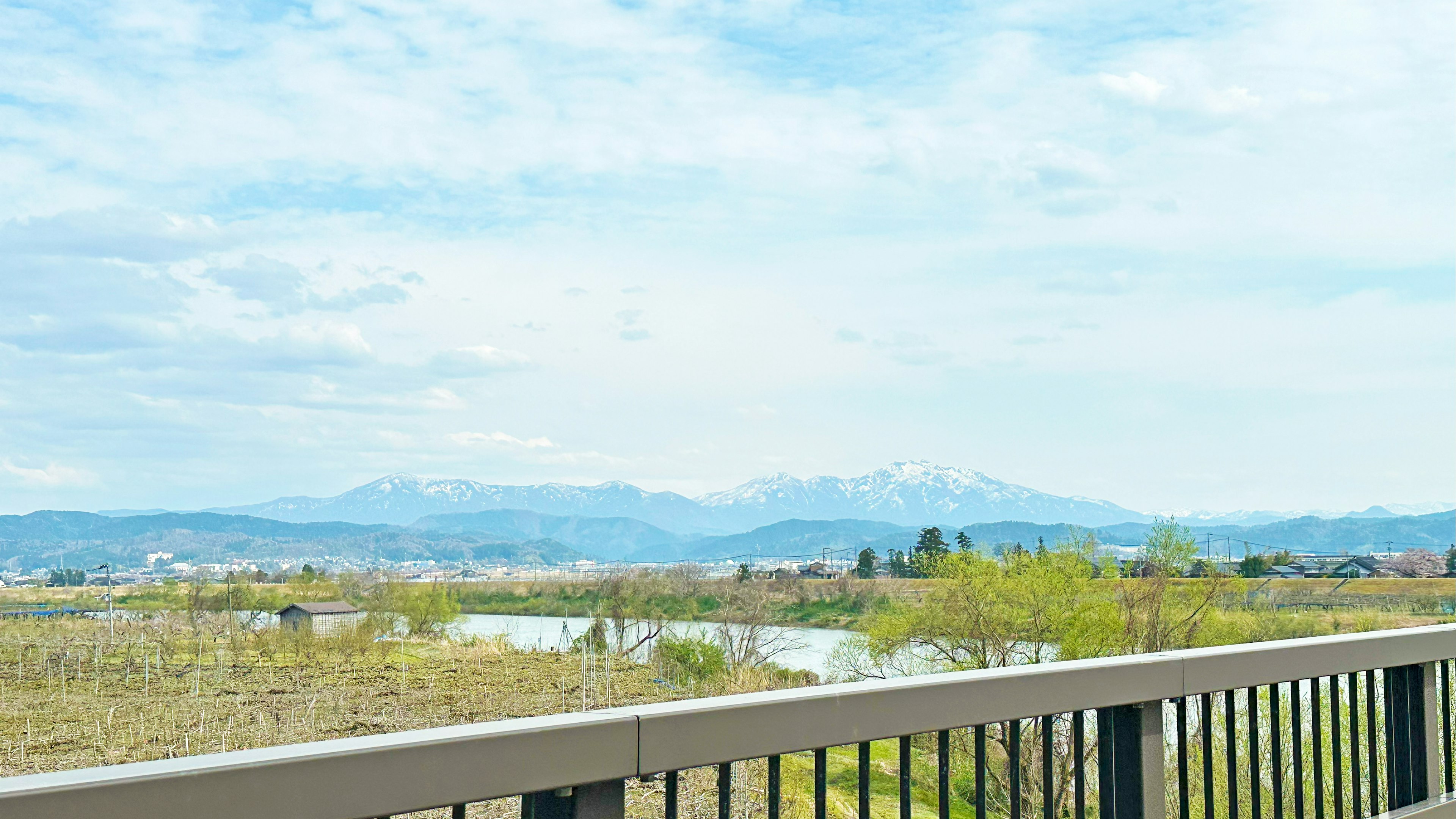 Vue panoramique sur des montagnes et une rivière sous un ciel bleu avec un garde-corps de balcon au premier plan