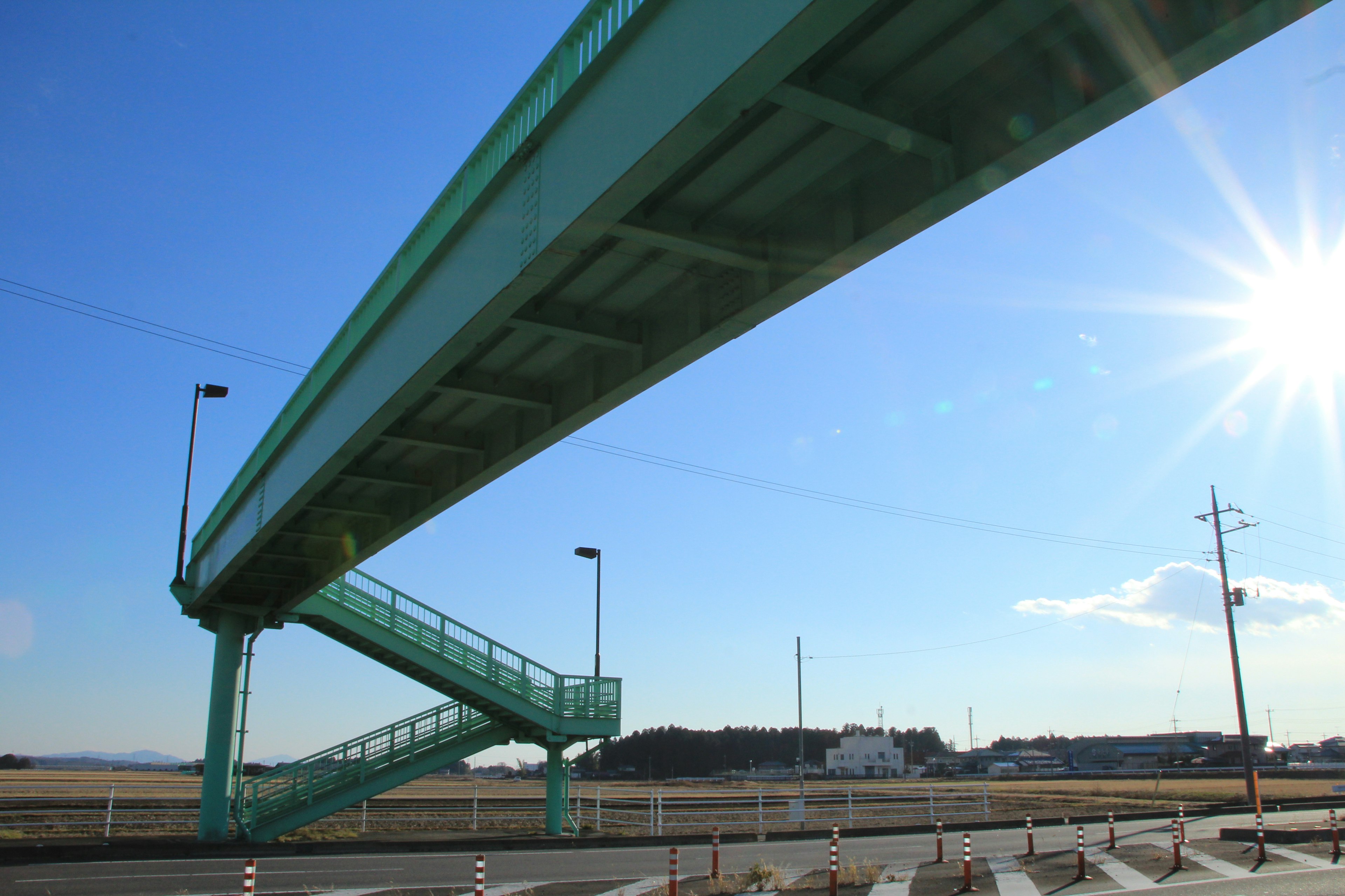 A green pedestrian bridge with stairs under a clear blue sky