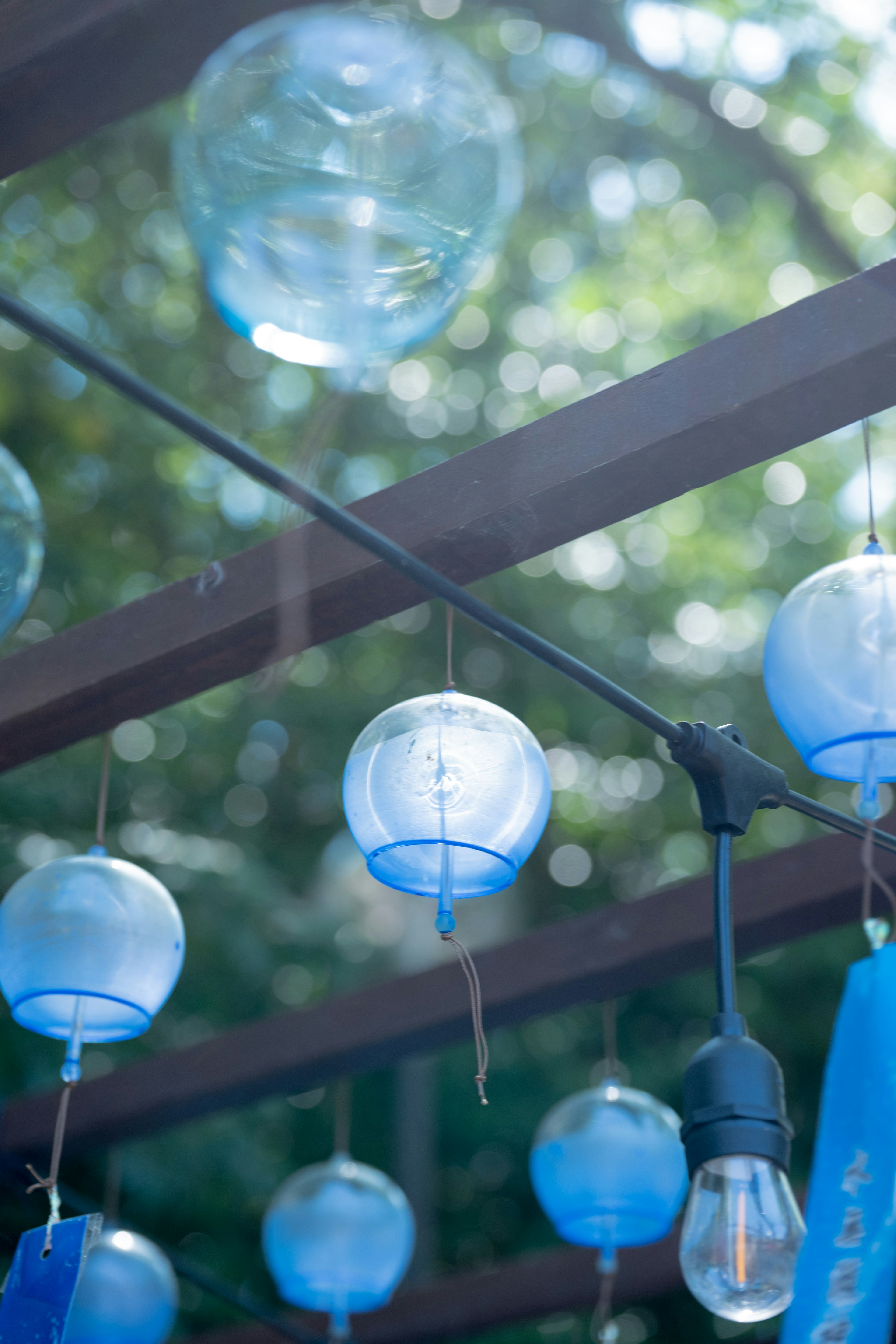 Scène extérieure avec des carillons éoliens bleus suspendus, lumière douce filtrant