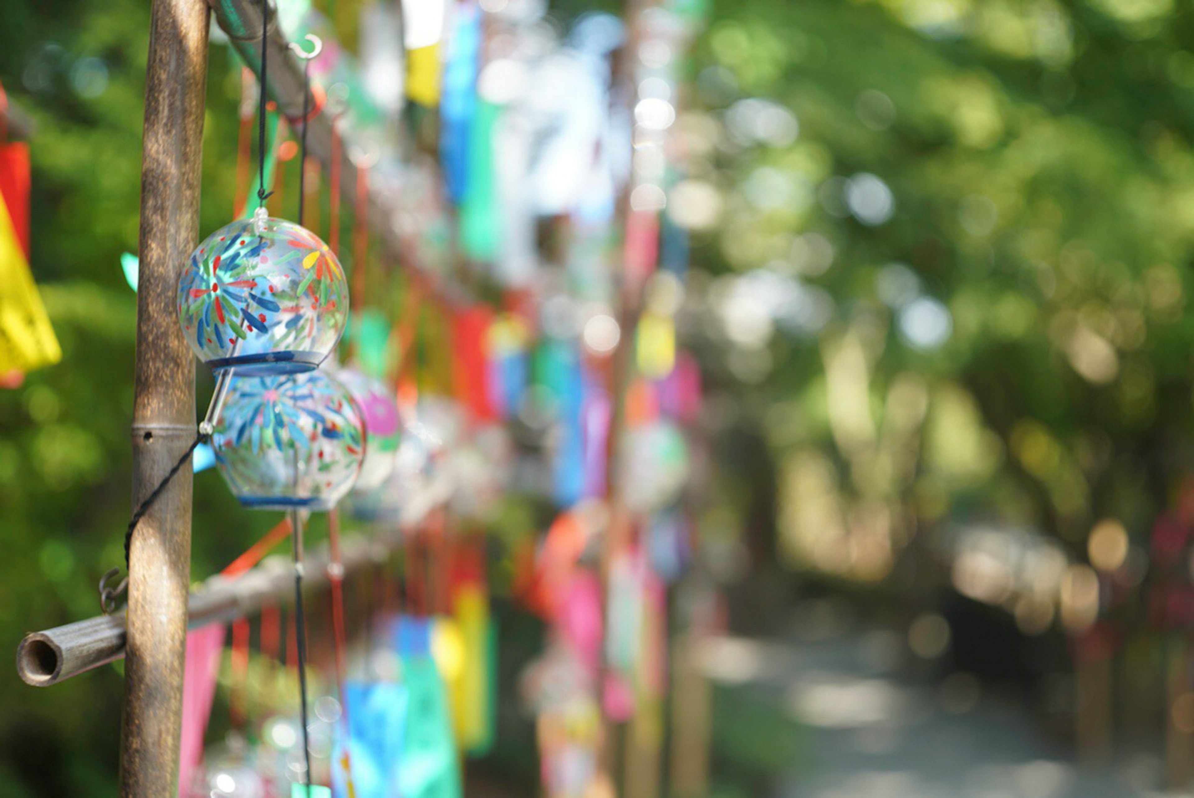 Colorful wind chimes hanging from a wooden pole with a blurred green background