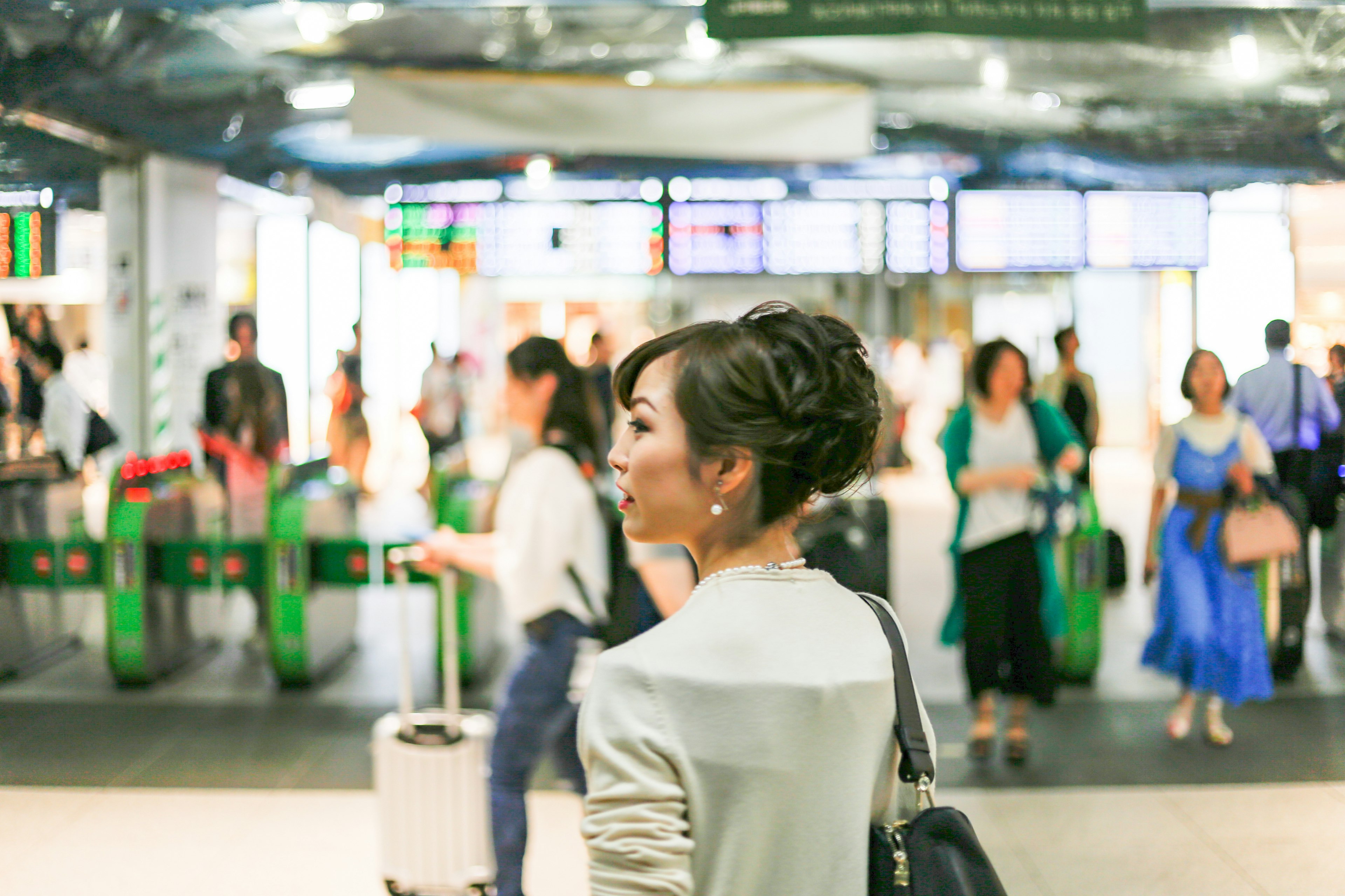 Woman in a light jacket walking toward a train station ticket gate with a crowd of travelers