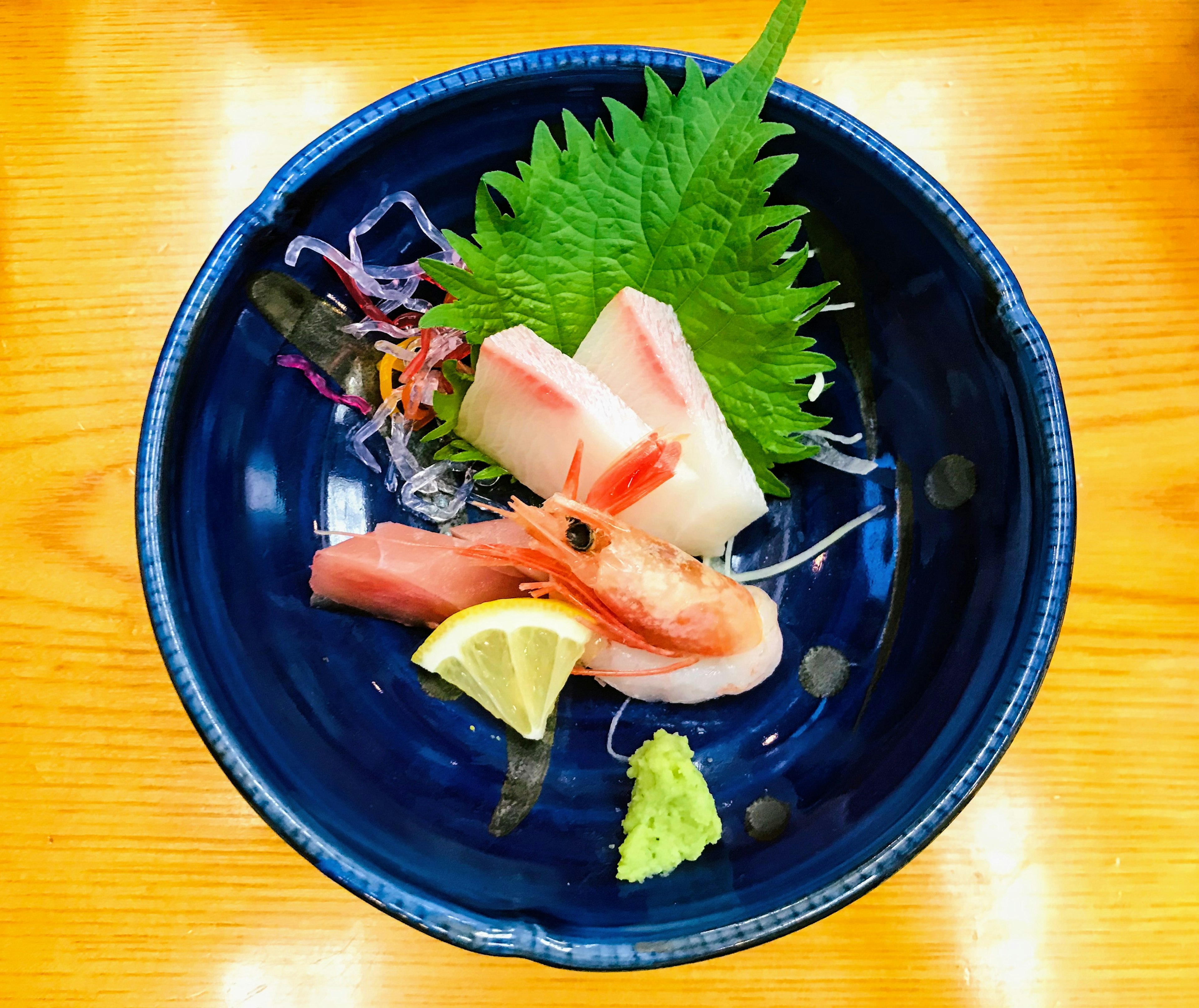 Sashimi frais servi sur une assiette bleue avec des feuilles de shiso