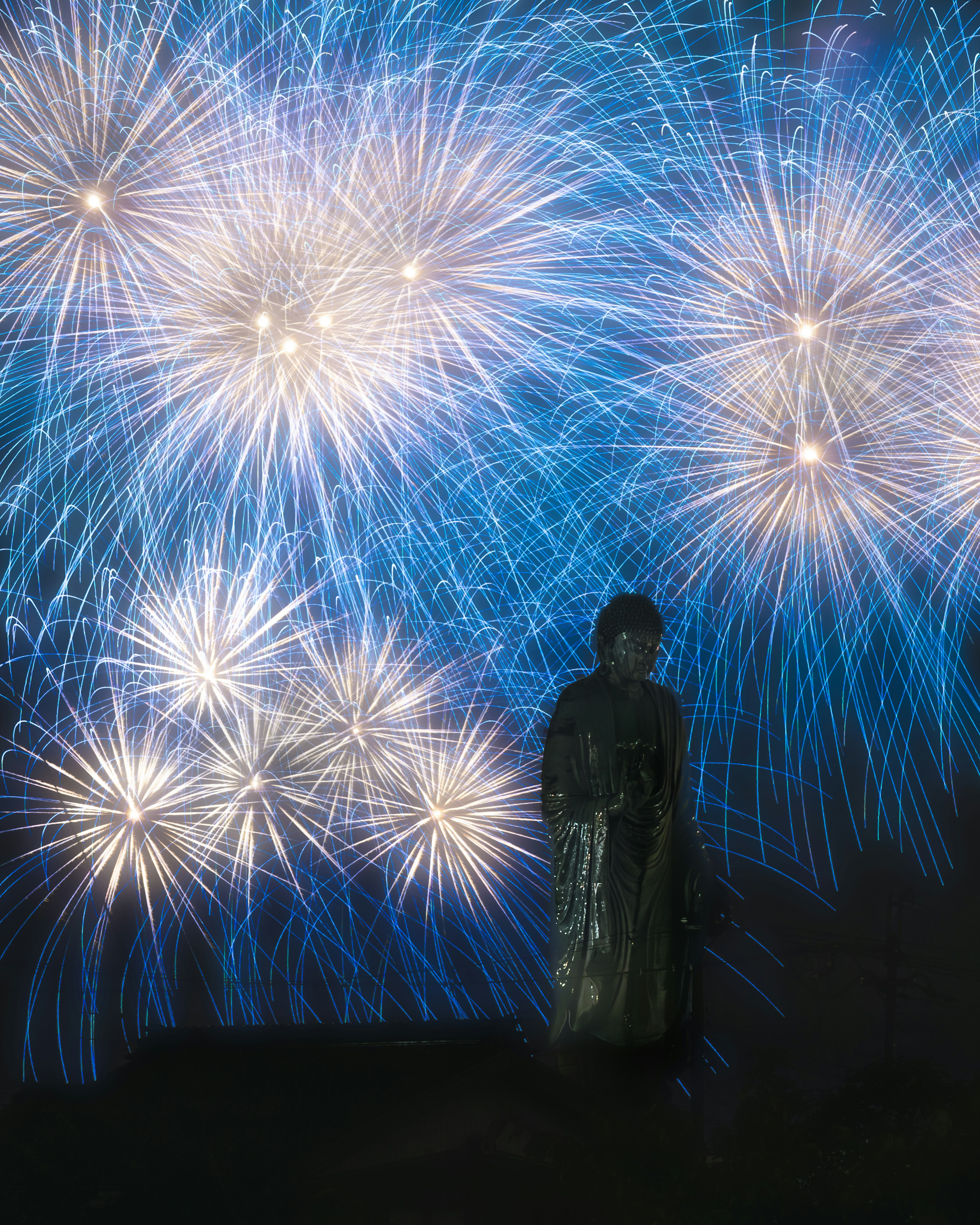 青い背景に花火が輝く中で立っている人物のシルエット