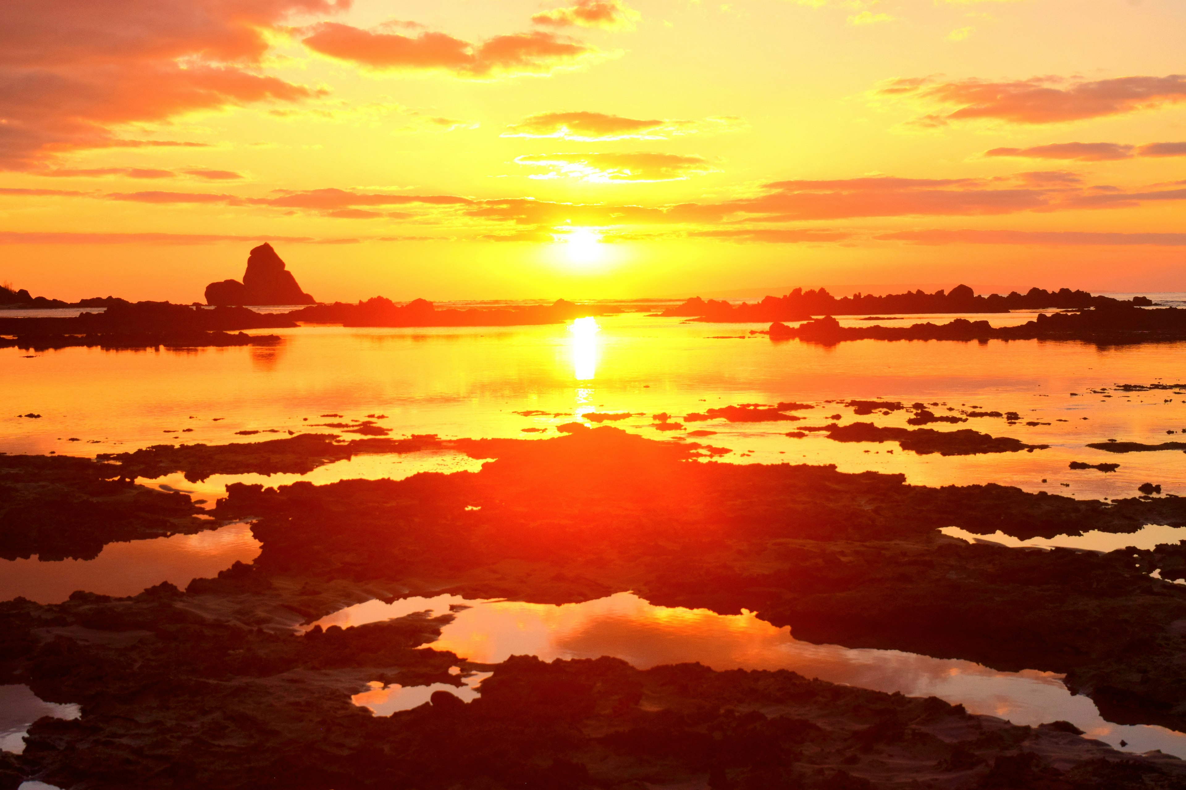 Stunning sunset over the ocean with rocks and pools reflecting the orange sky